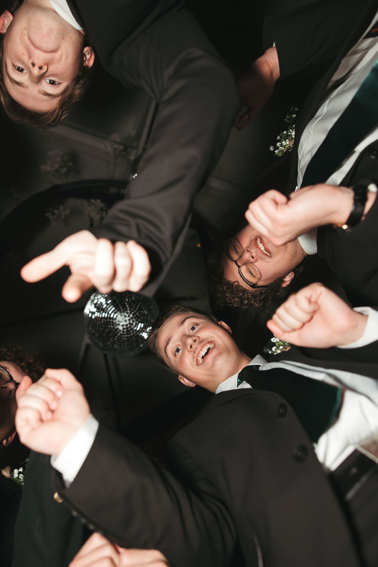 Fun circular photo of wedding party members looking down at camera with joyful expressions.