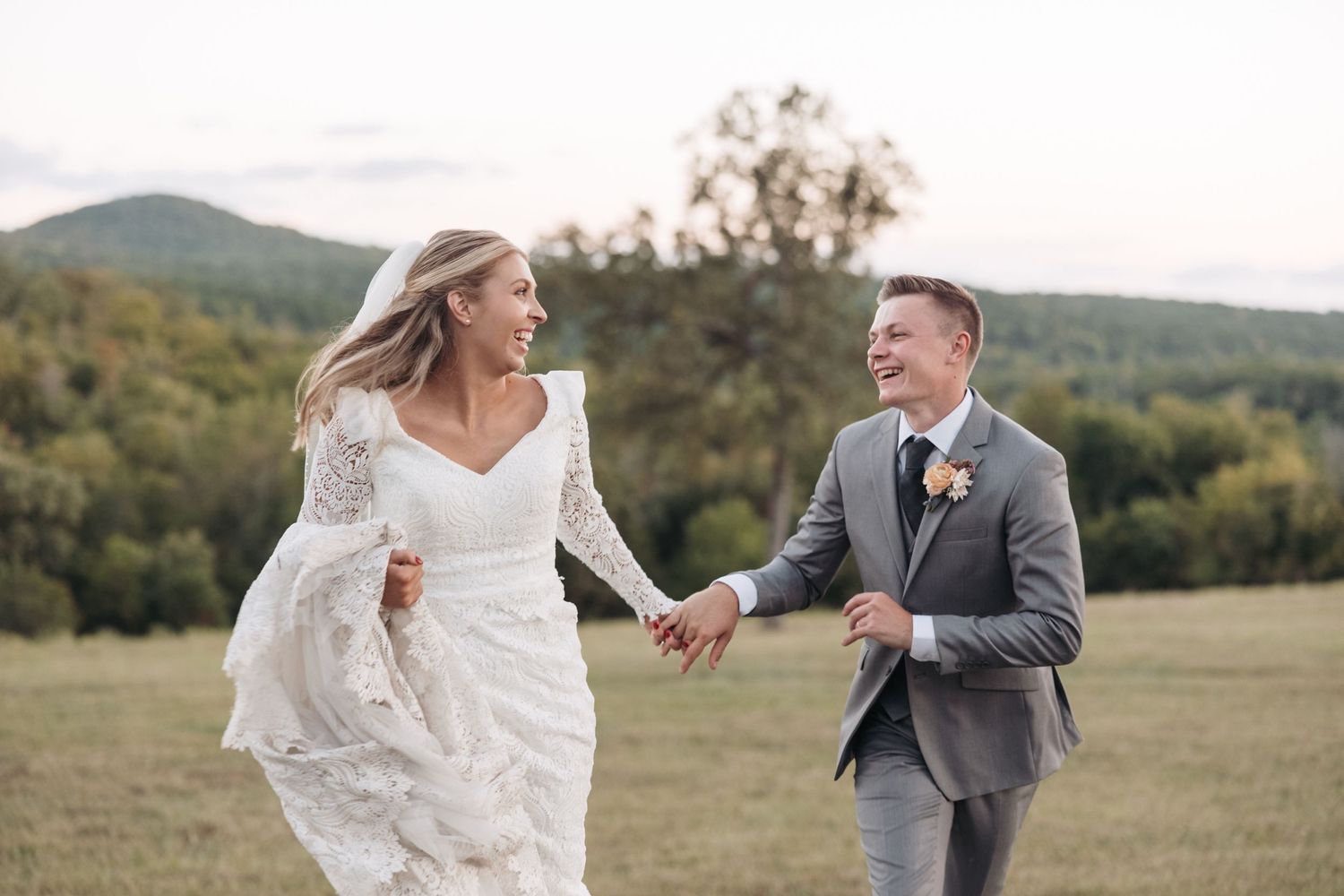 Newlyweds run joyfully hand-in-hand through a scenic field during their outdoor wedding photo session.