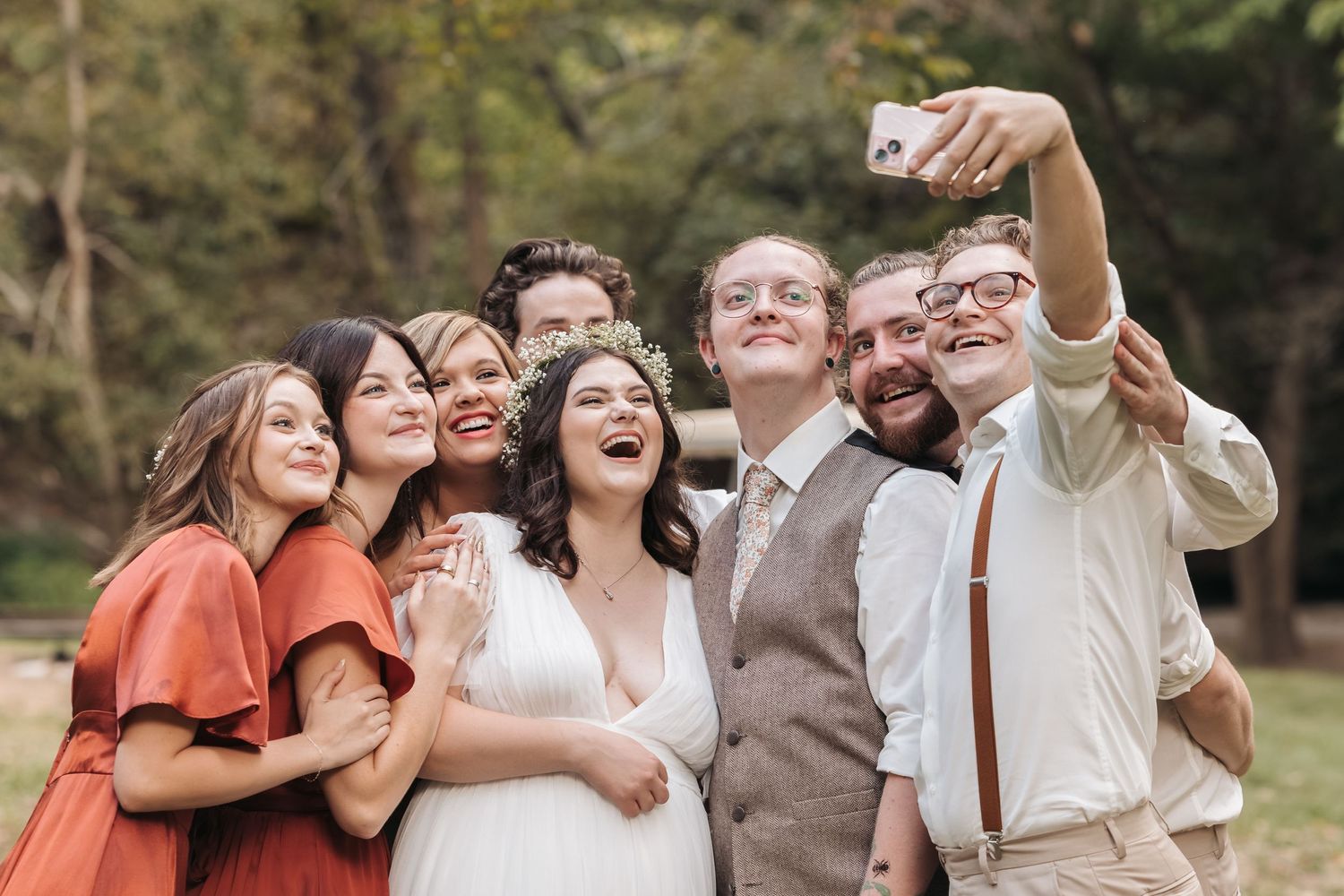 Group taking celebratory selfie at outdoor wedding.