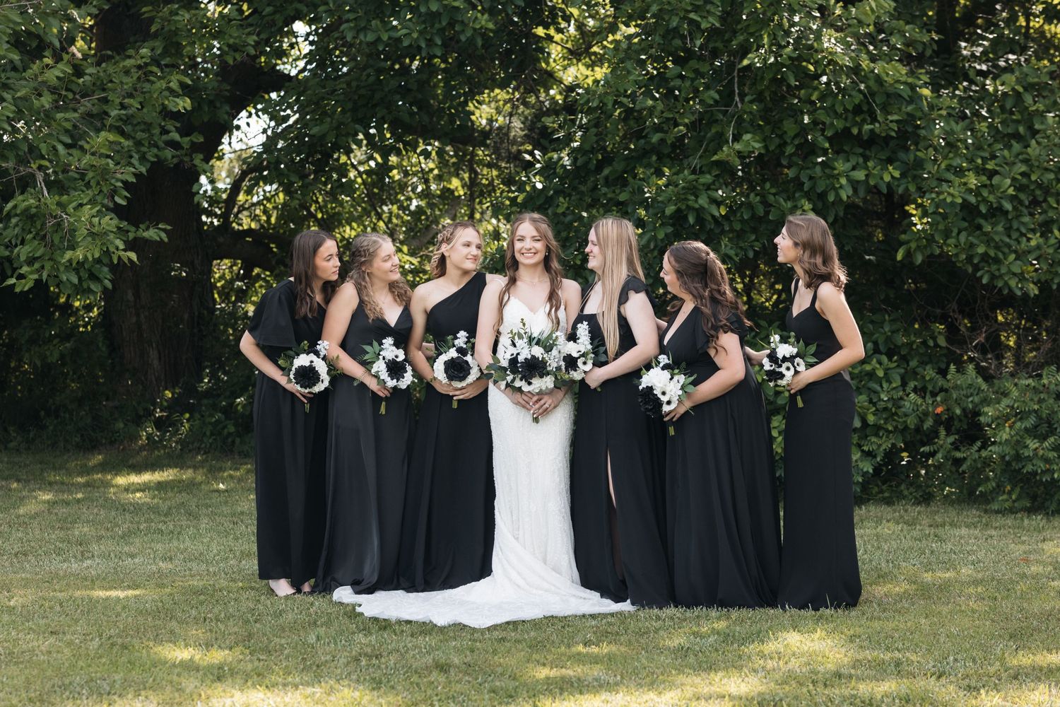 Wedding party poses for formal photo with bride in white gown centered among bridesmaids in black dresses.