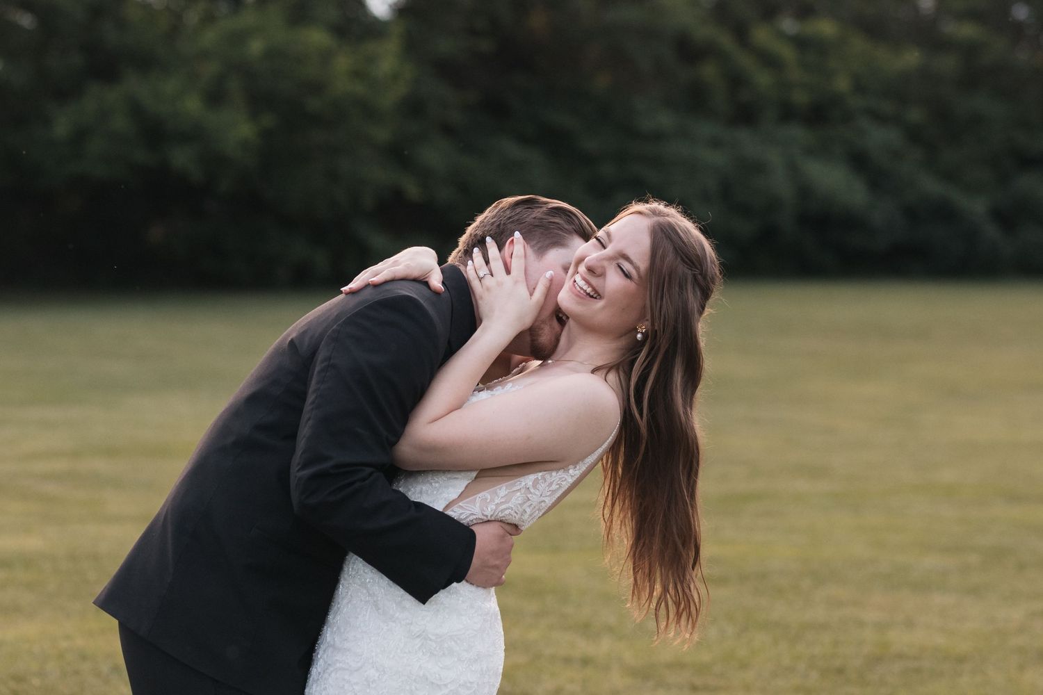 A joyful wedding couple embraces in a grassy field during an intimate outdoor photoshoot.