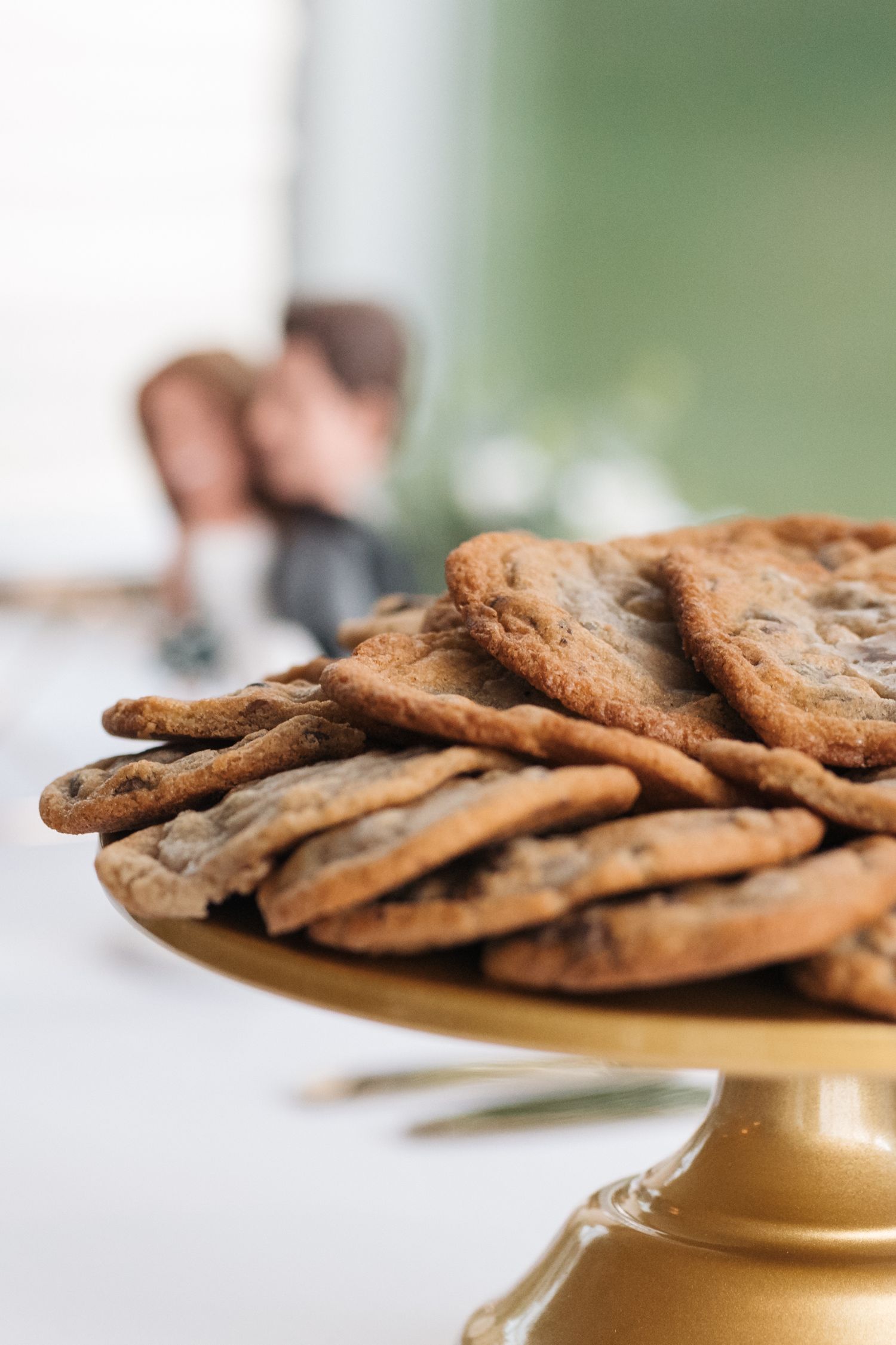 Fresh chocolate chip cookies displayed on a gold cake stand at a wedding reception.