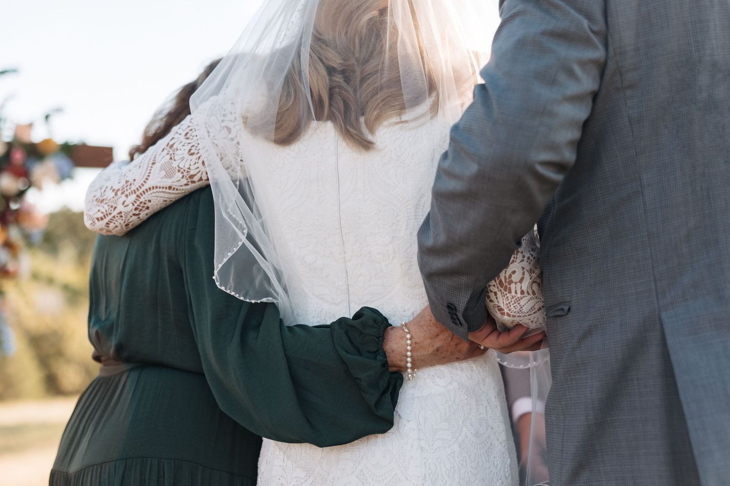 Intimate side view of wedding couple embracing during outdoor ceremony.