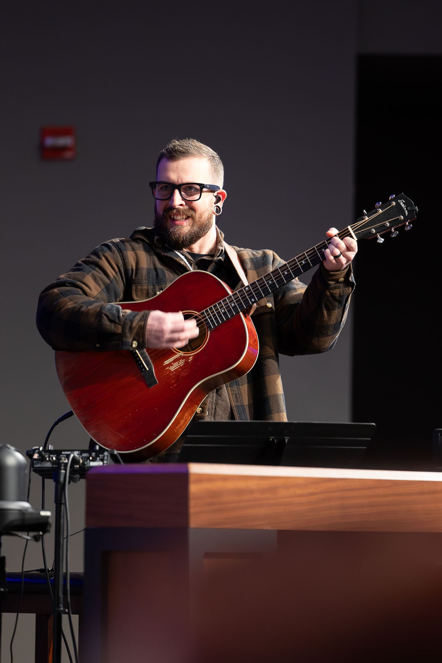 Musician plays red acoustic guitar while performing on stage.