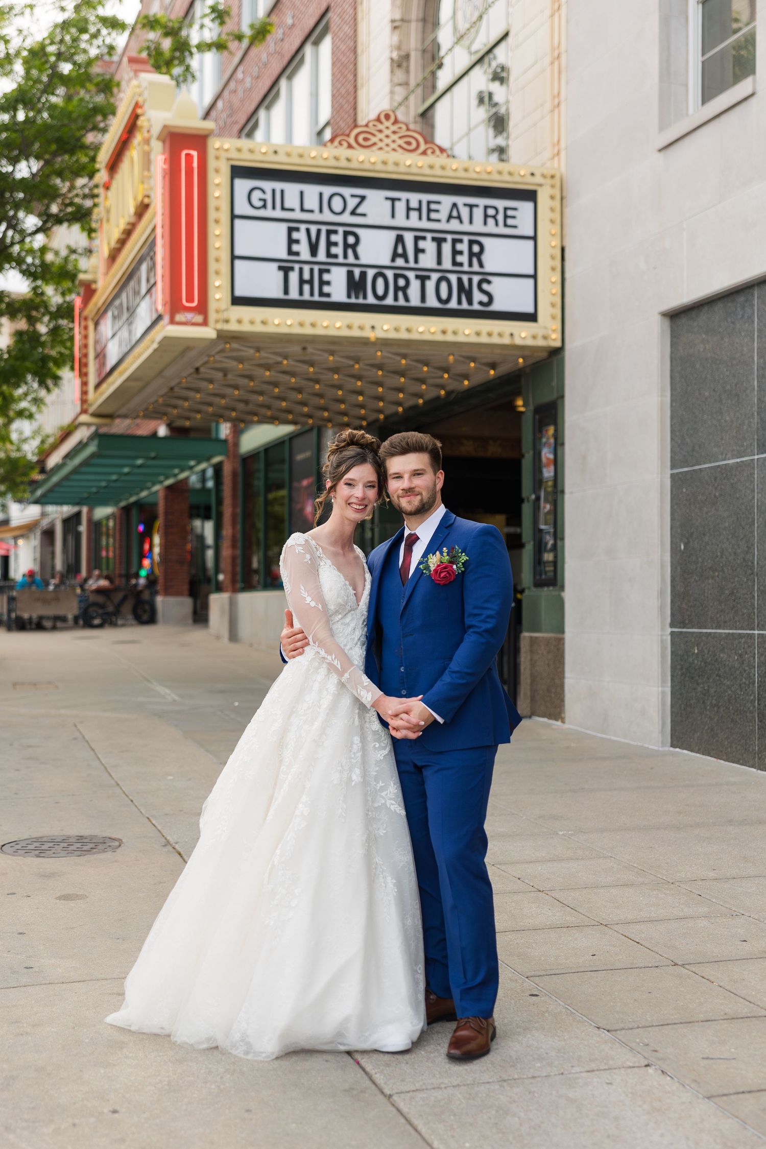 Bride and groom pose in front of Gillioz Theatre marquee reading Ever After The Mortons on wedding day.