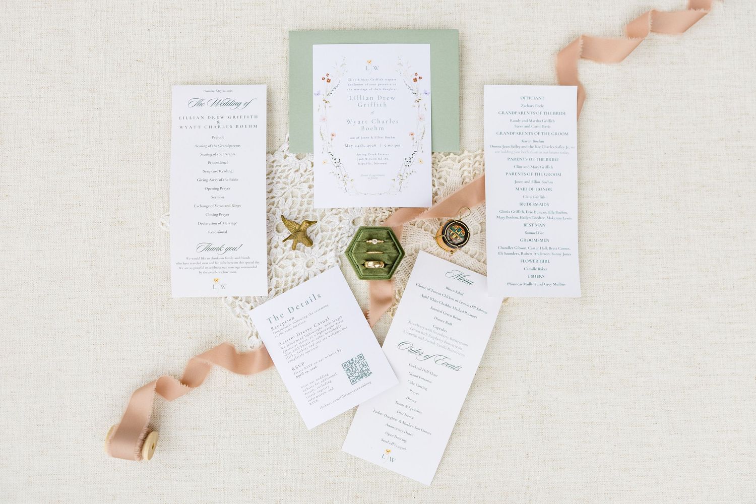 Elegant wedding invitation suite with sage green card, floral details, wax seal, ring box, and blush ribbon on linen.