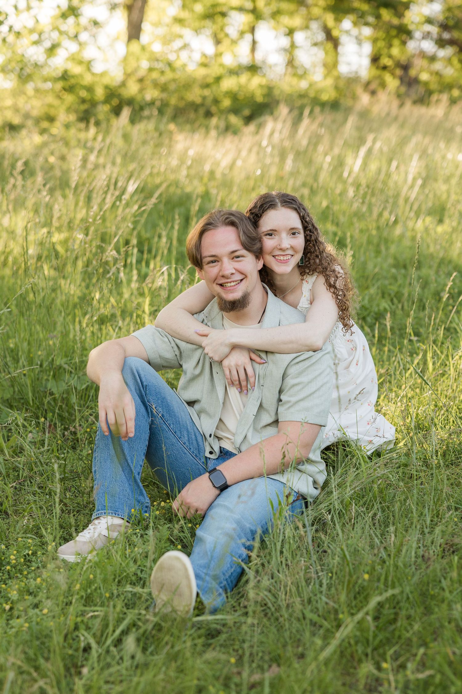 People sitting together in a grassy meadow during golden hour wearing casual clothing and smiling at the camera.