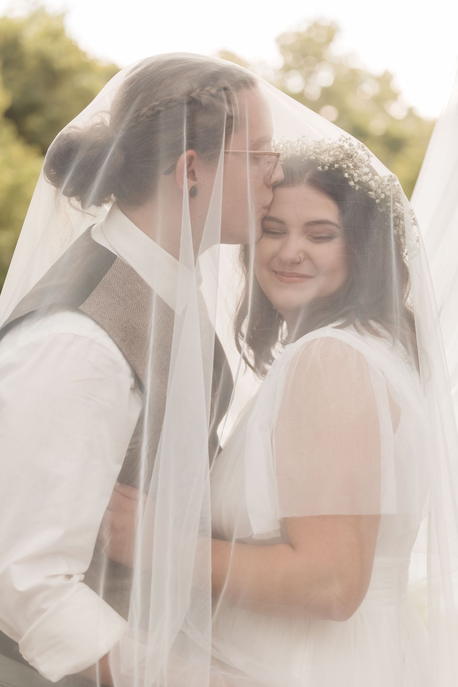 Intimate wedding moment captured under flowing veil in natural lighting.