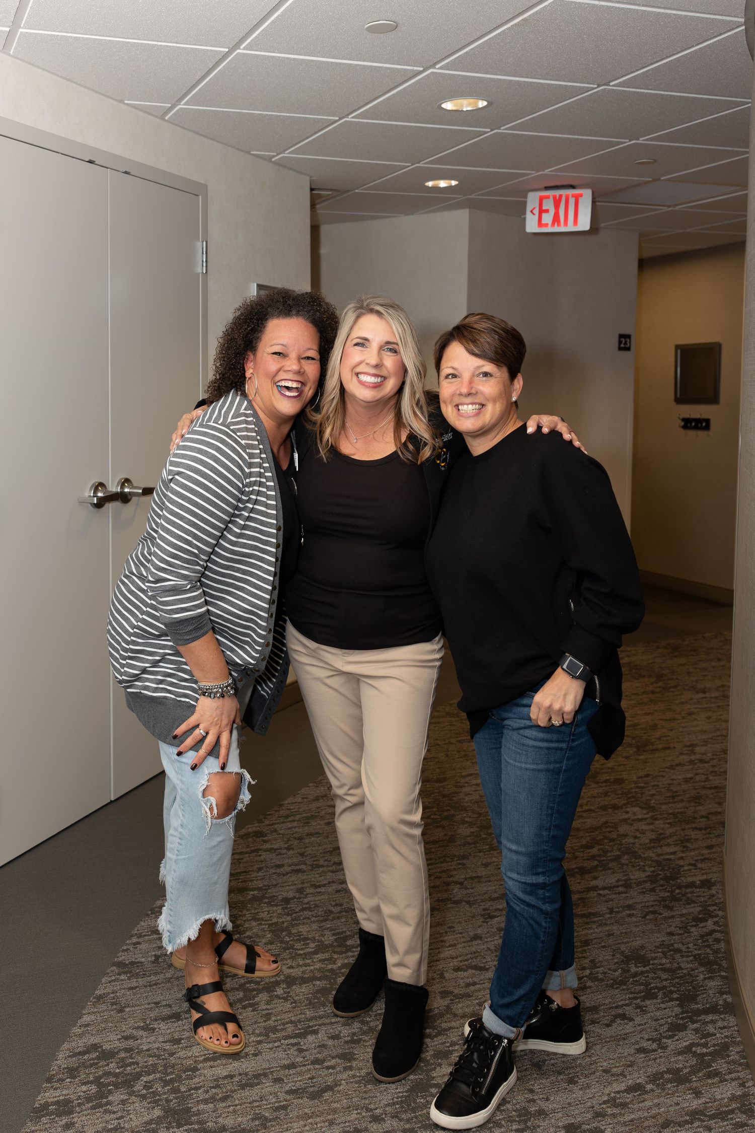 Three friends posing together in a hallway at a corporate event with casual business attire.
