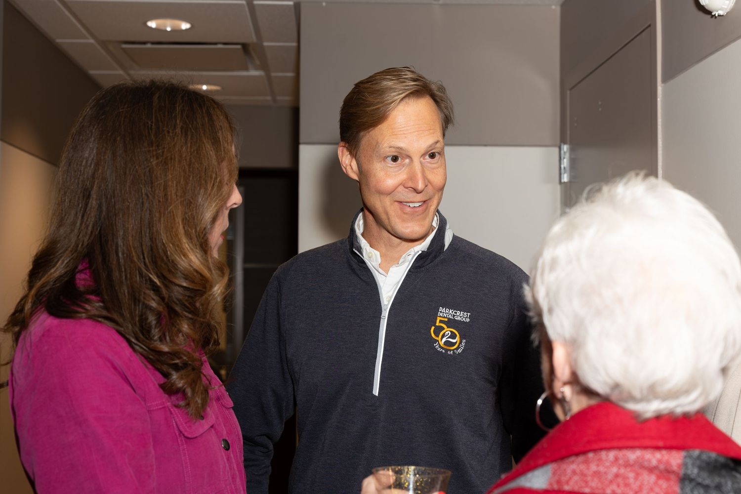 Person in navy quarter-zip pullover speaking with others at indoor event.
