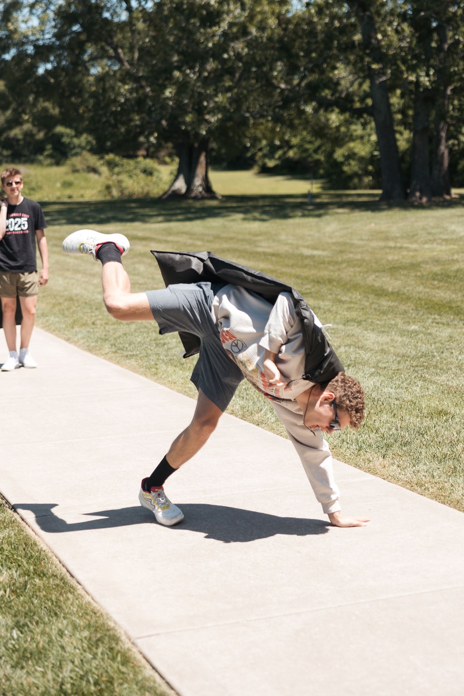A person performs a dramatic backbend on a concrete path in a grassy park setting.