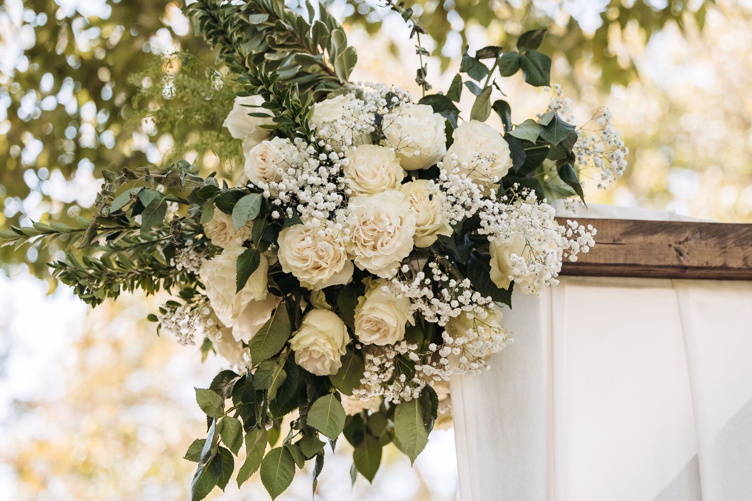 Elegant white floral arrangement with roses and baby's breath decorating a wedding arch.