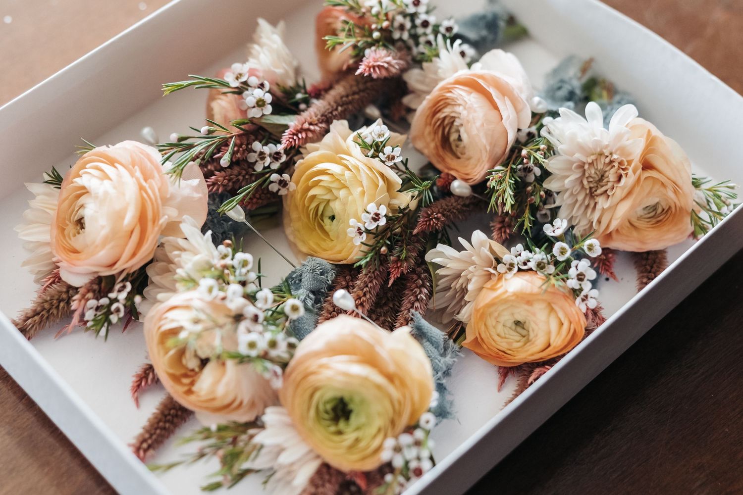 Delicate peach and cream ranunculus boutonnieres with baby's breath in a white box.