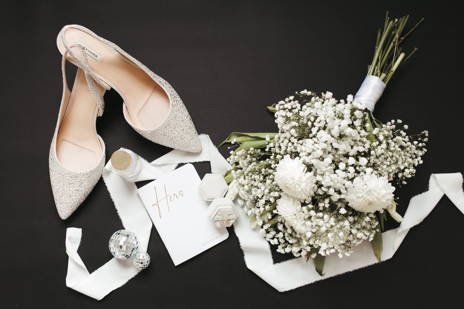 Elegant bridal shoes paired with a white floral bouquet and ribbon on dark surface.