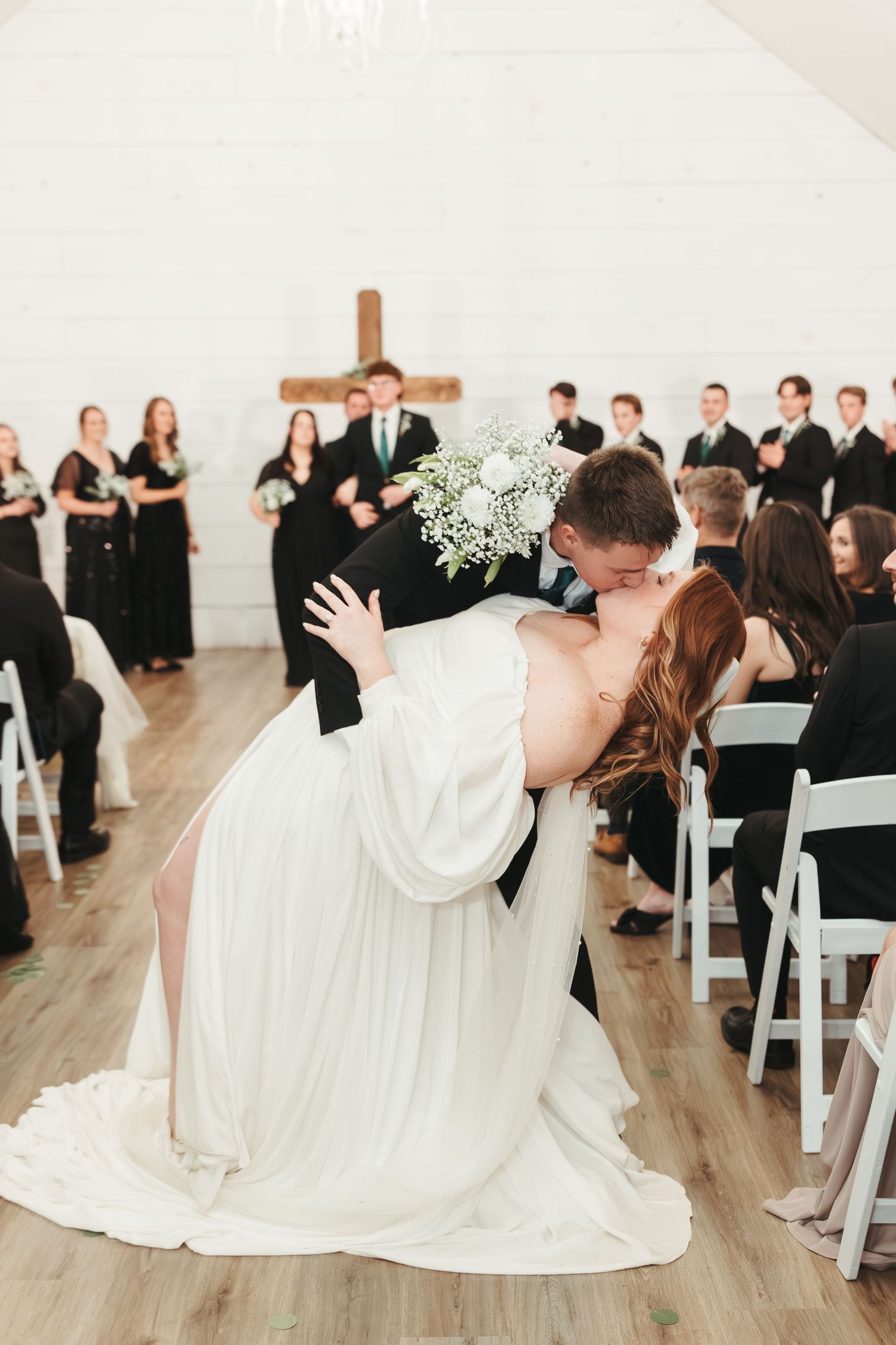 A romantic dip kiss during a wedding ceremony with guests and wedding party looking on.