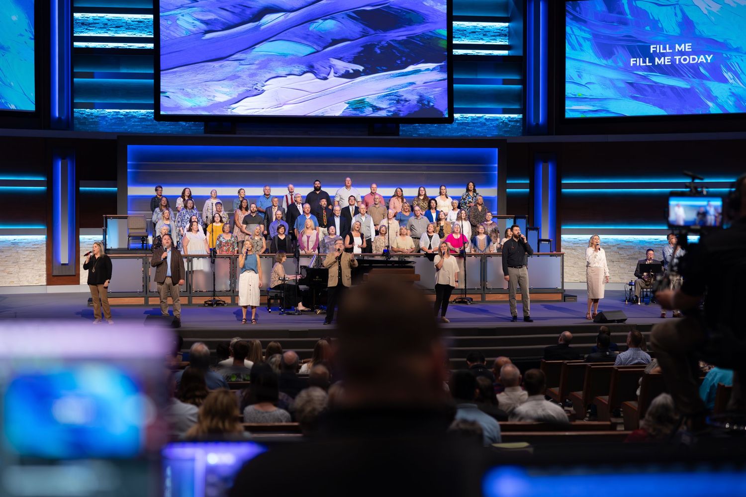 Church worship team performs on stage with blue screens and lighting effects.