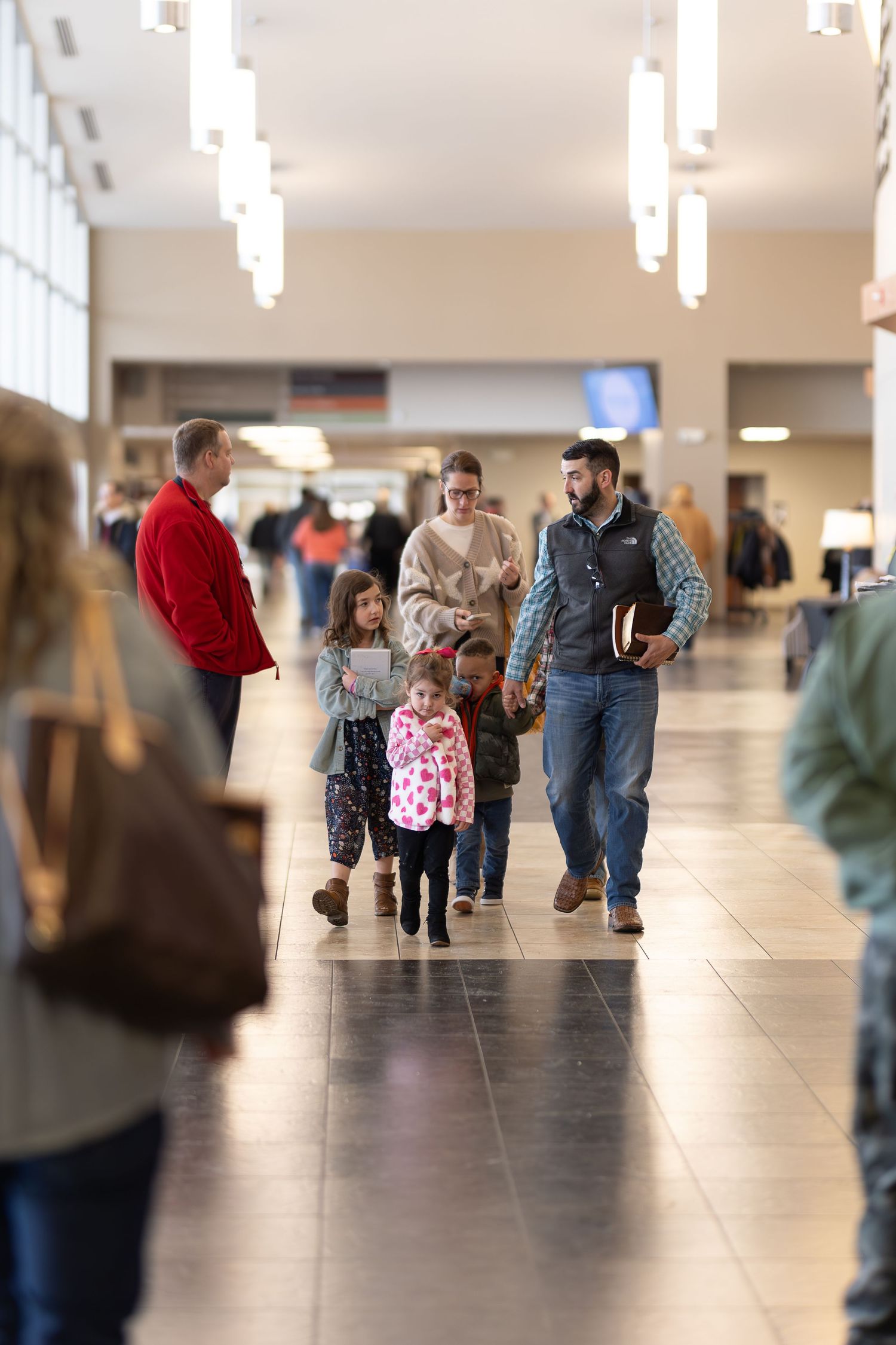 Families walking together through modern building hallway with overhead lighting.