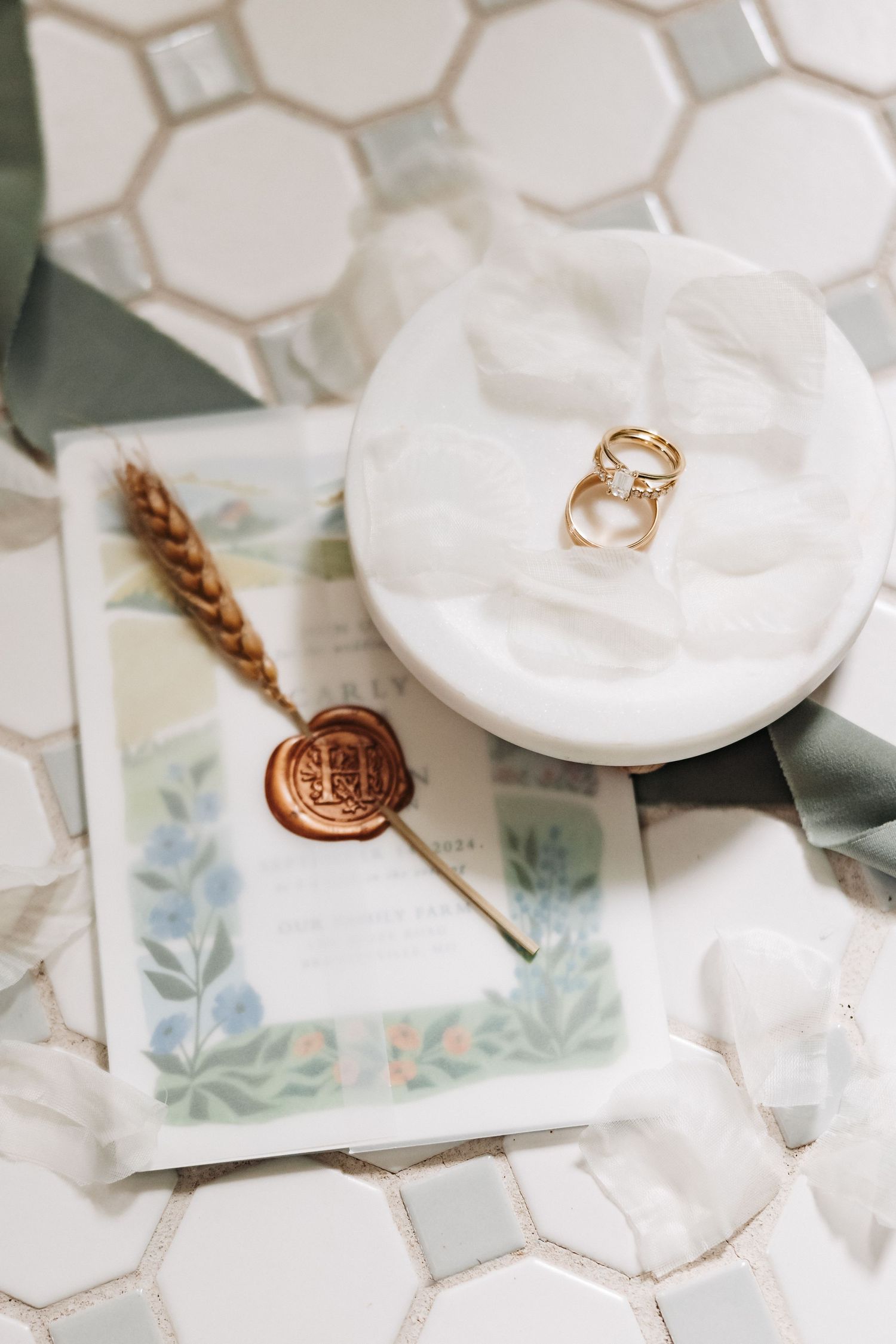 Wedding rings displayed on white ceramic with a vintage wax seal and floral tile background.