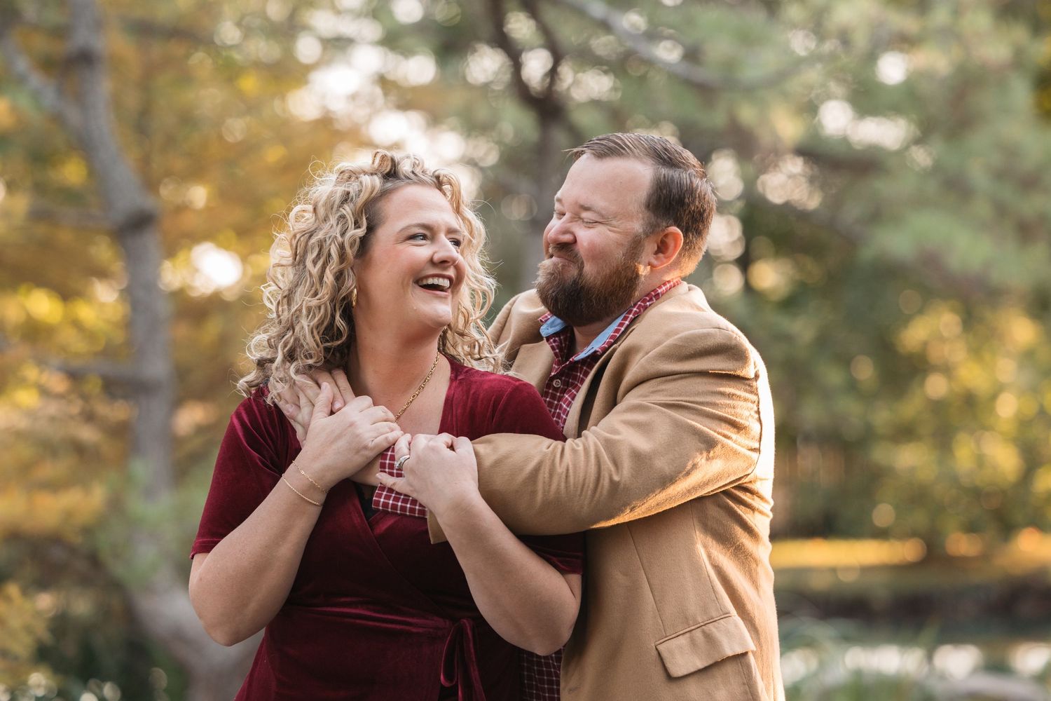 A couple shares a joyful laugh together in an autumn forest setting.