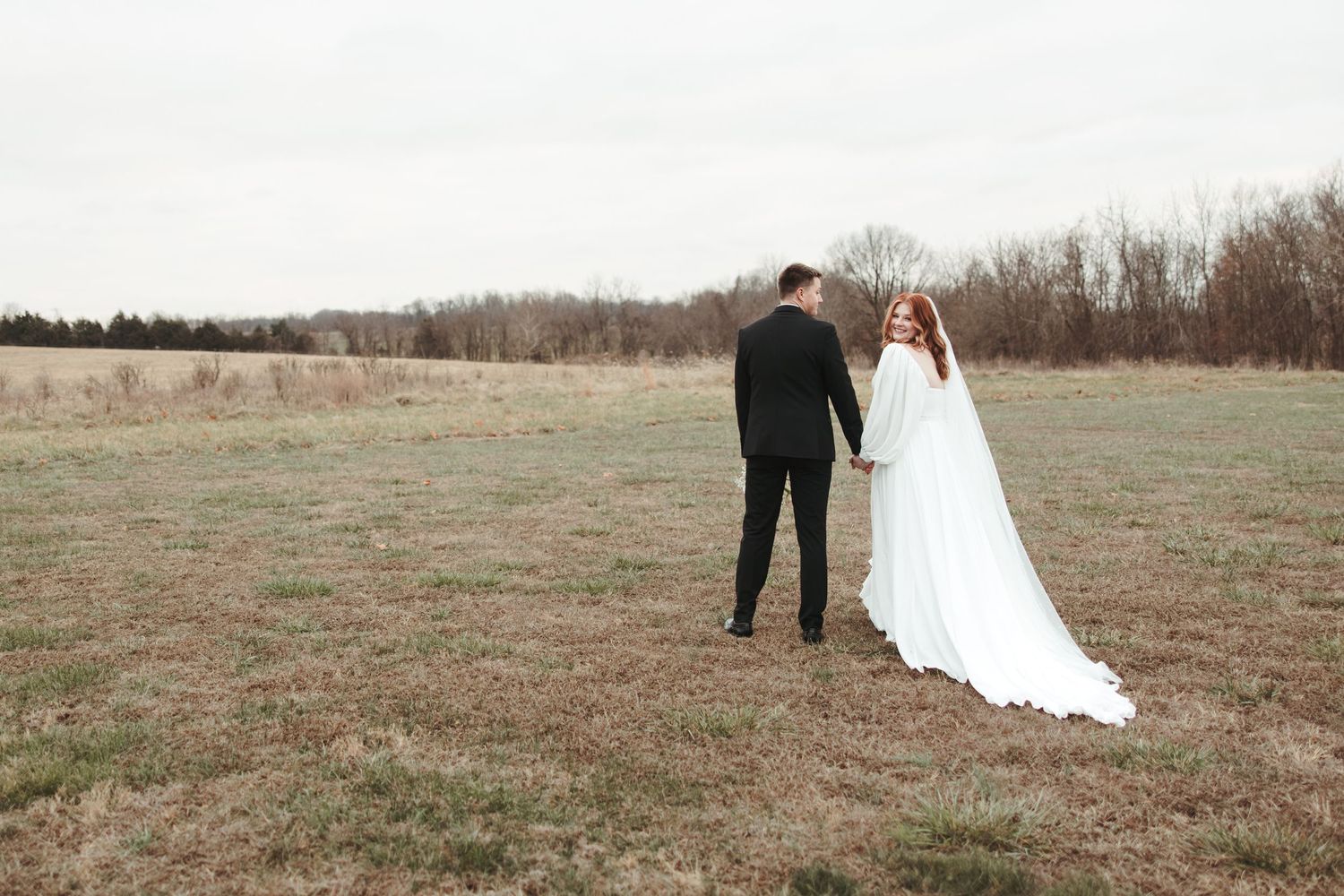 Wedding couple stands together in an open field on their special day.