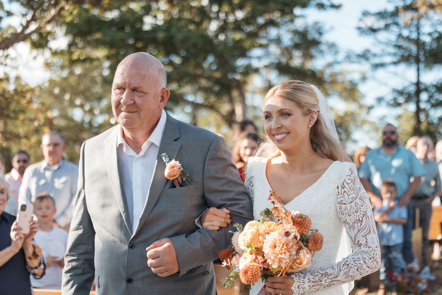 Wedding procession walking down aisle at outdoor ceremony with peach bouquet.