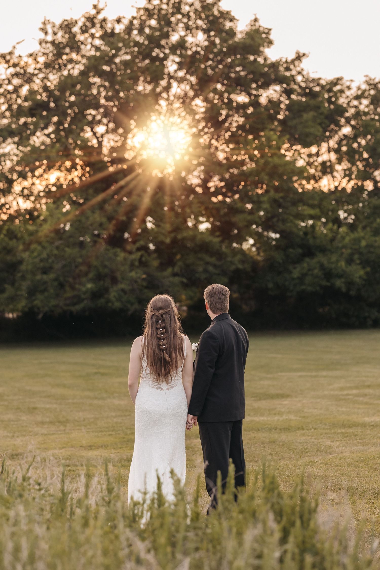 Newlyweds stand silhouetted against a stunning sunset in a peaceful meadow.