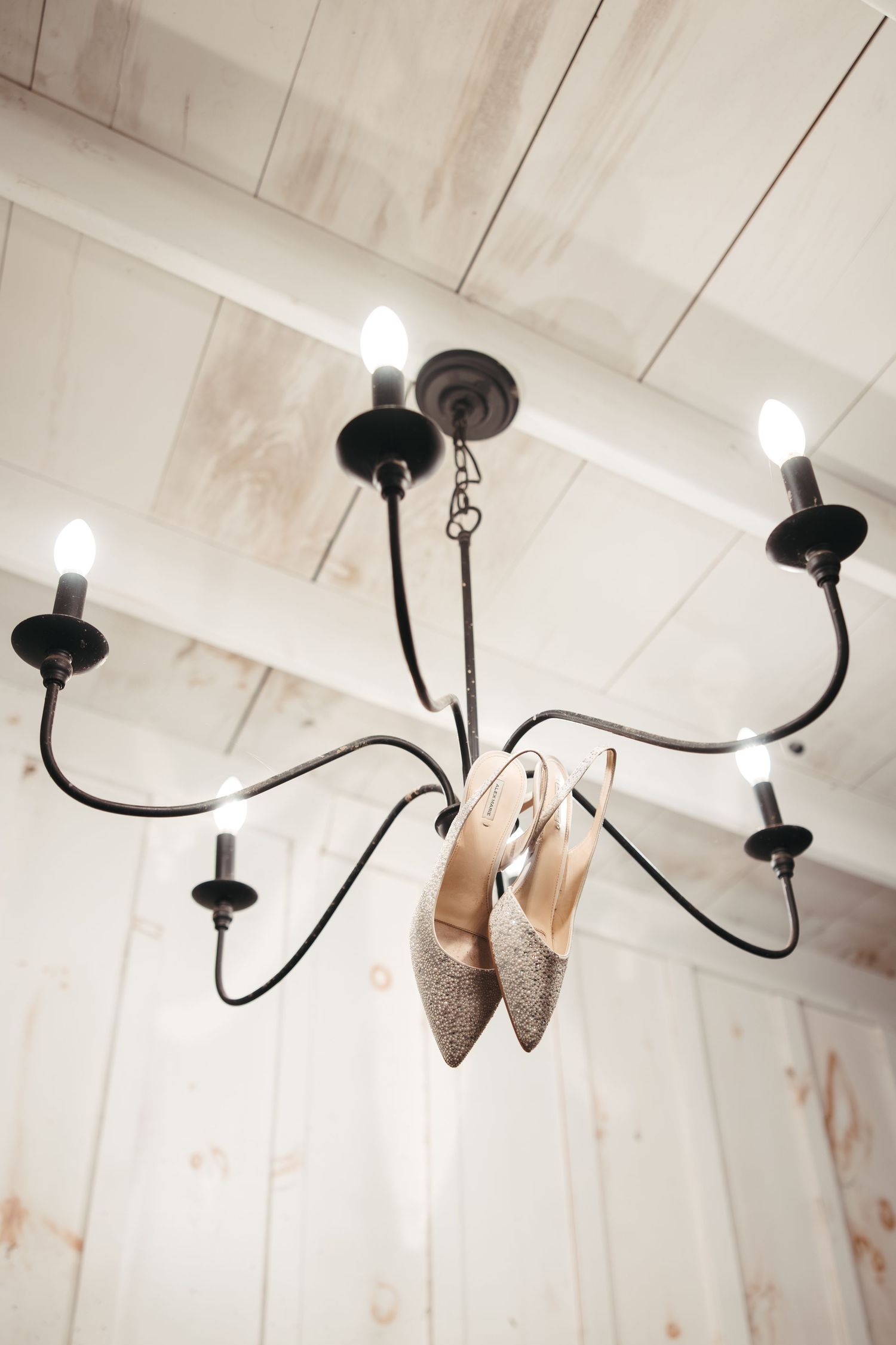 A pair of sparkly gold high heel shoes hanging from a black chandelier with white lights.