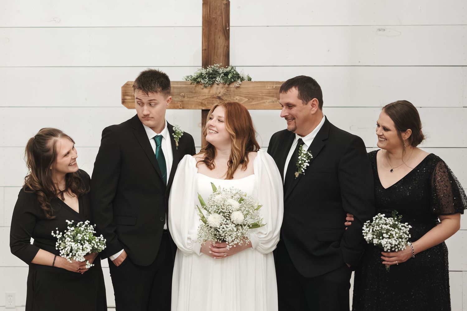 A wedding party poses against a white wall with rustic wooden beam detail.