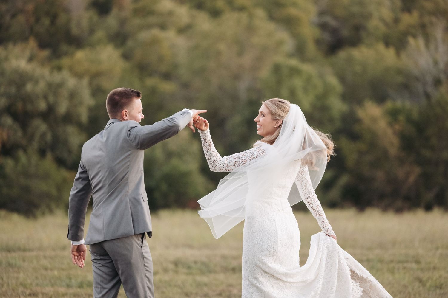 Bride and groom twirl and dance together in a scenic meadow during wedding photoshoot.
