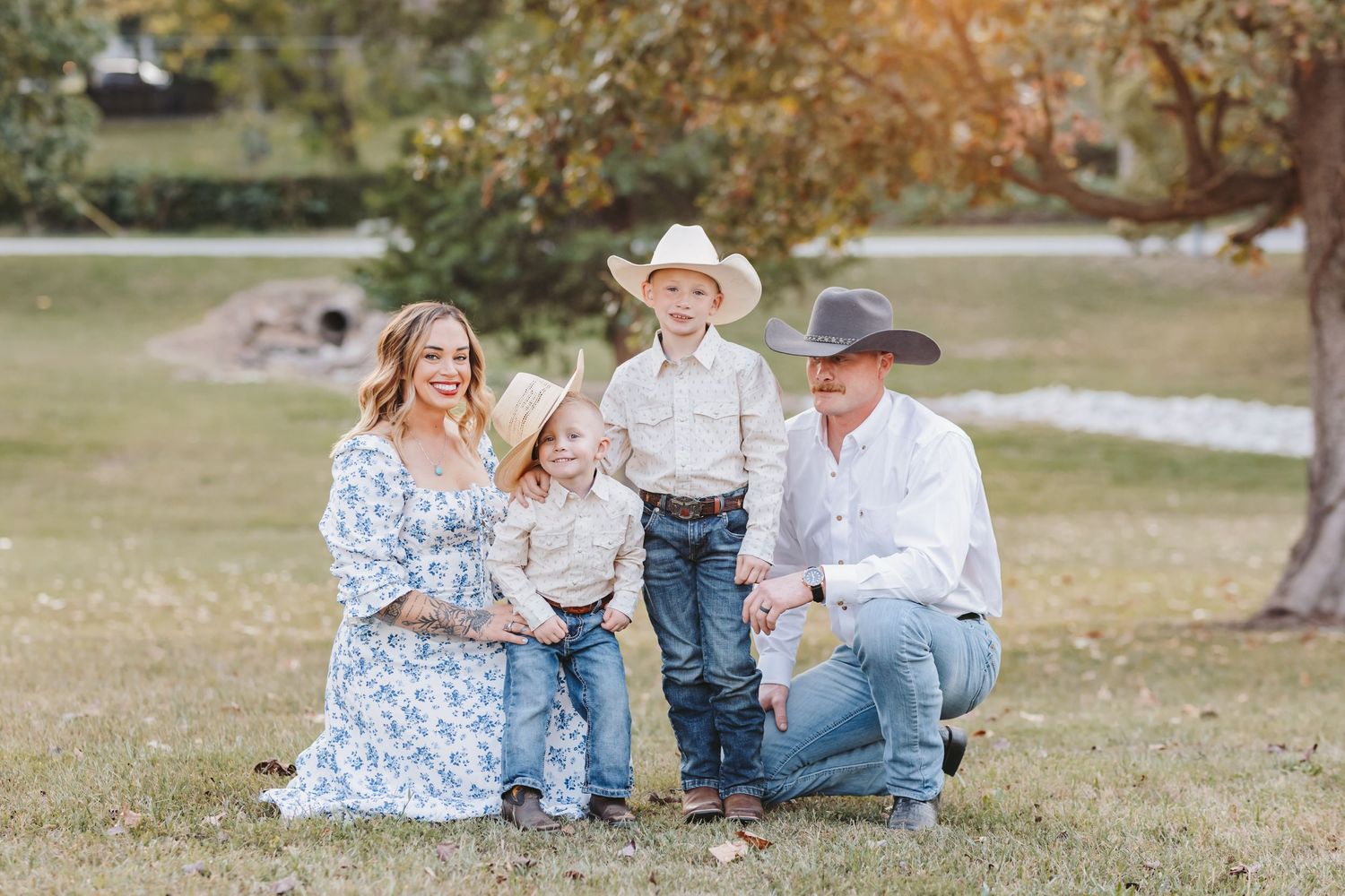 A western-styled family portrait taken in a grassy park with mature trees.