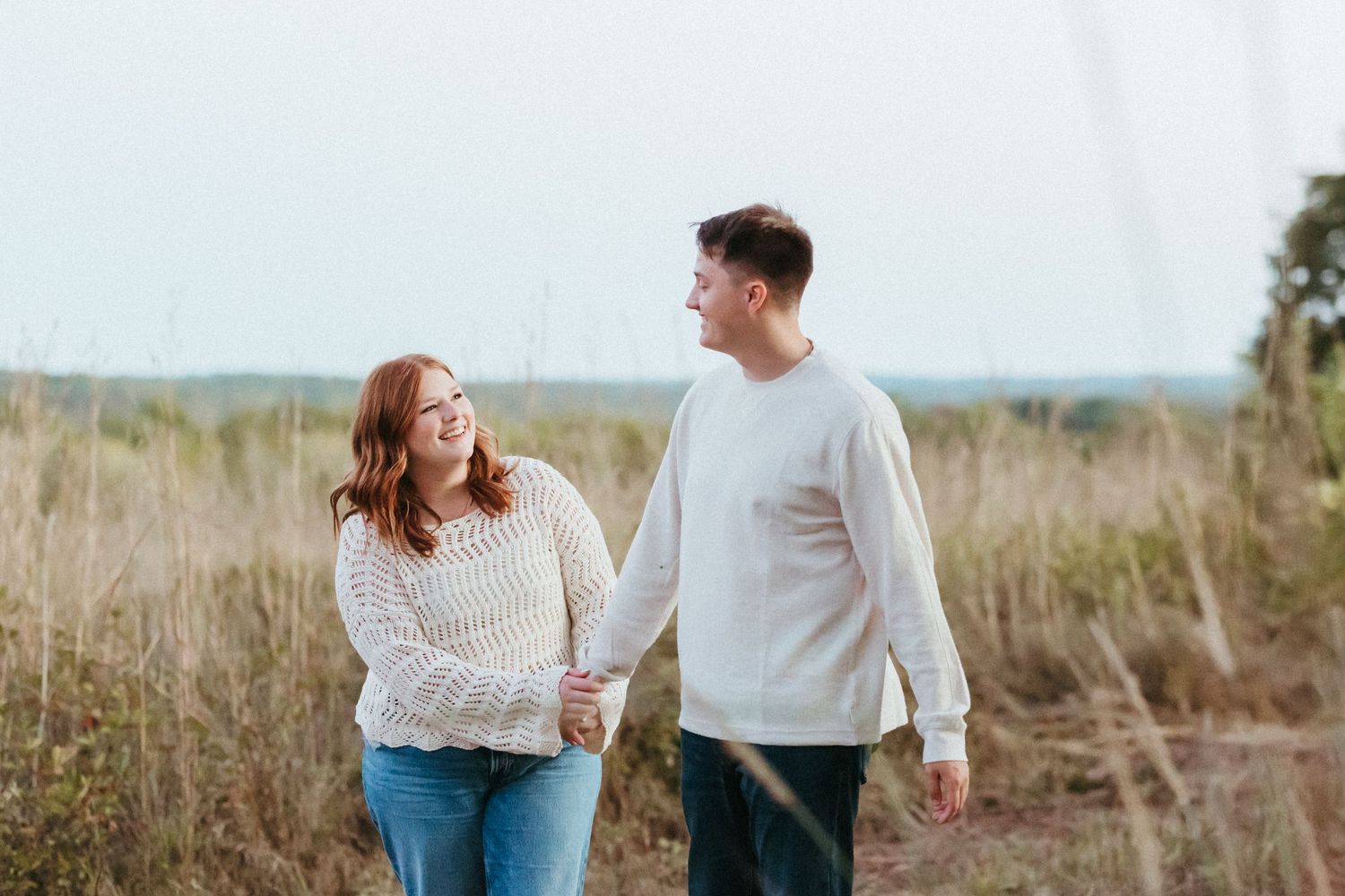 A couple shares a joyful moment while walking through a natural field setting.