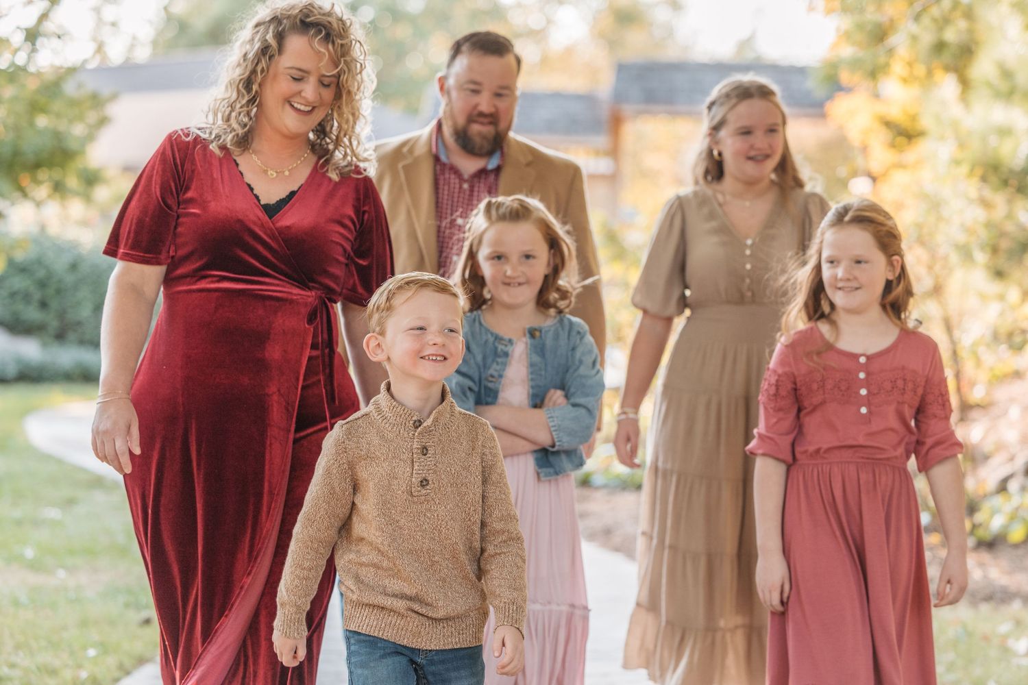 Family portrait outdoors wearing coordinated burgundy and neutral fall outfits.