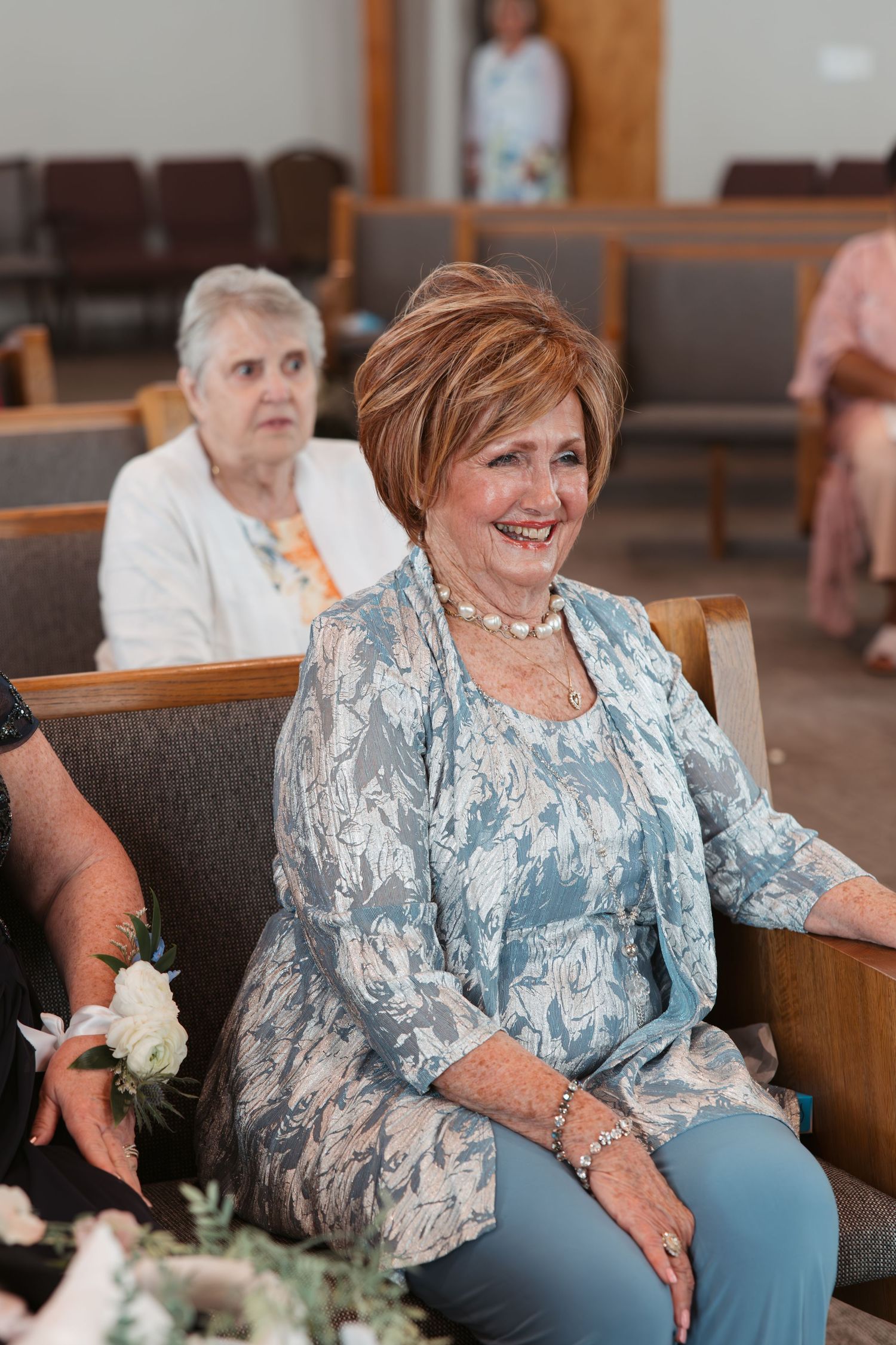 Wedding guest in light blue lace ensemble smiles while seated in church pew.