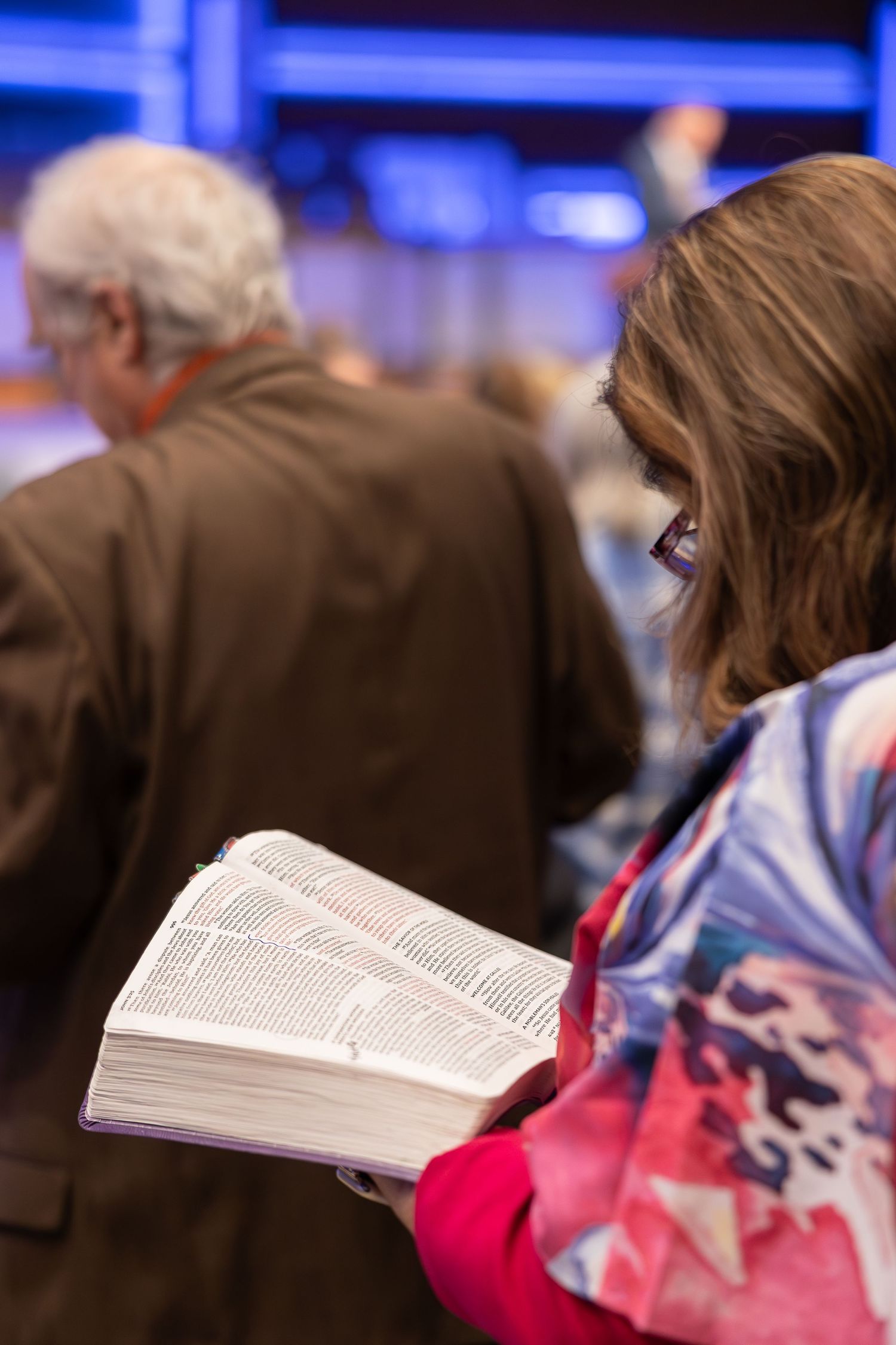 Person reading from open Bible during church service while seated in pew.