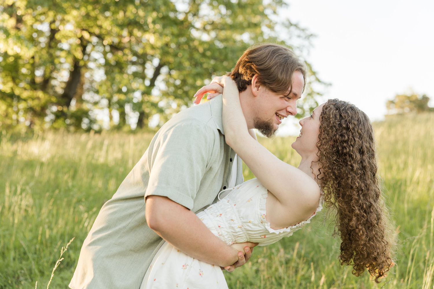 Romantic couple sharing an intimate moment in a sunlit meadow with green trees in the background.