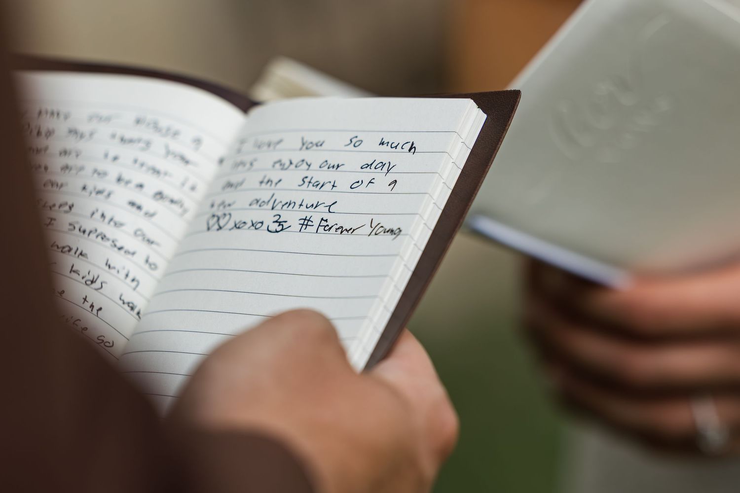 Hands holding open a small notebook with handwritten notes in blue ink on lined pages.