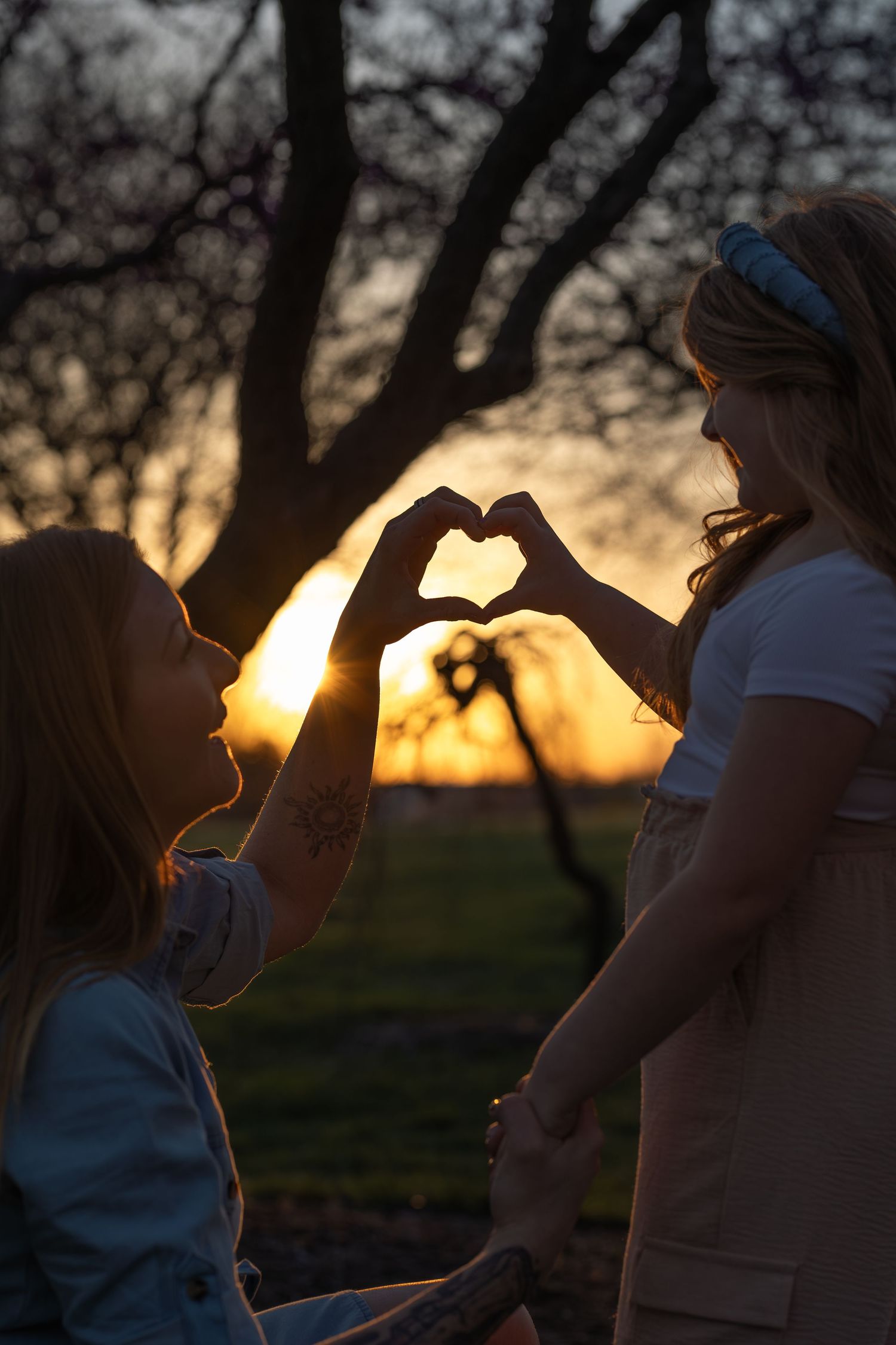People silhouetted against a warm sunset sky while making hand gestures in a serene outdoor setting.
