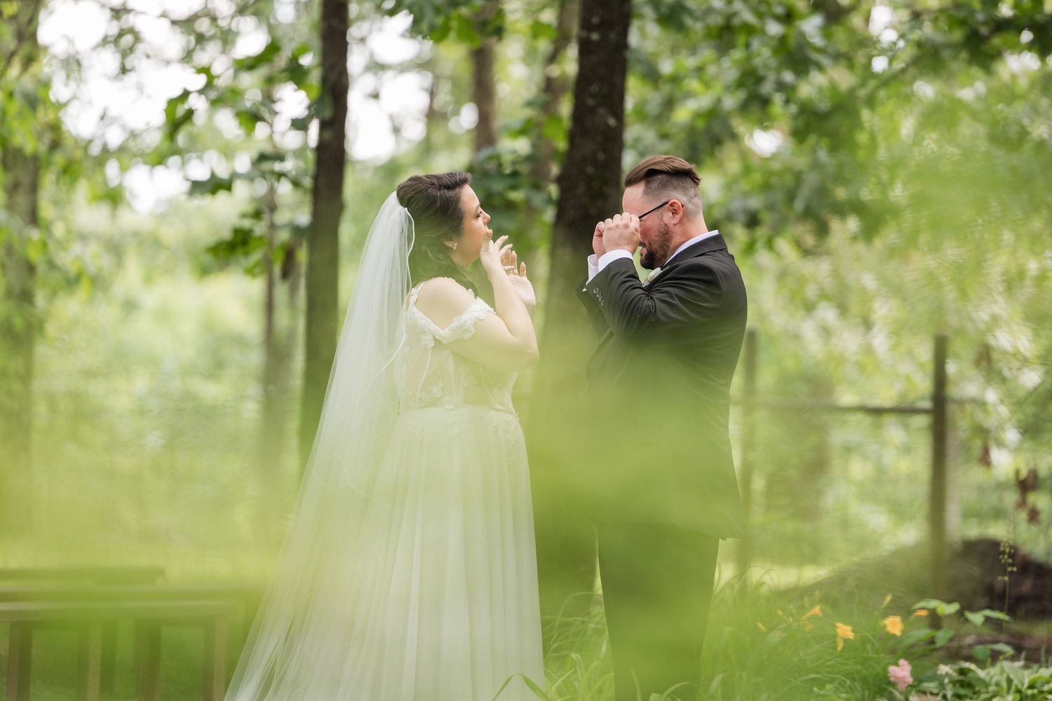 Bride and groom share an emotional first look moment surrounded by lush green trees in an outdoor woodland wedding setting.