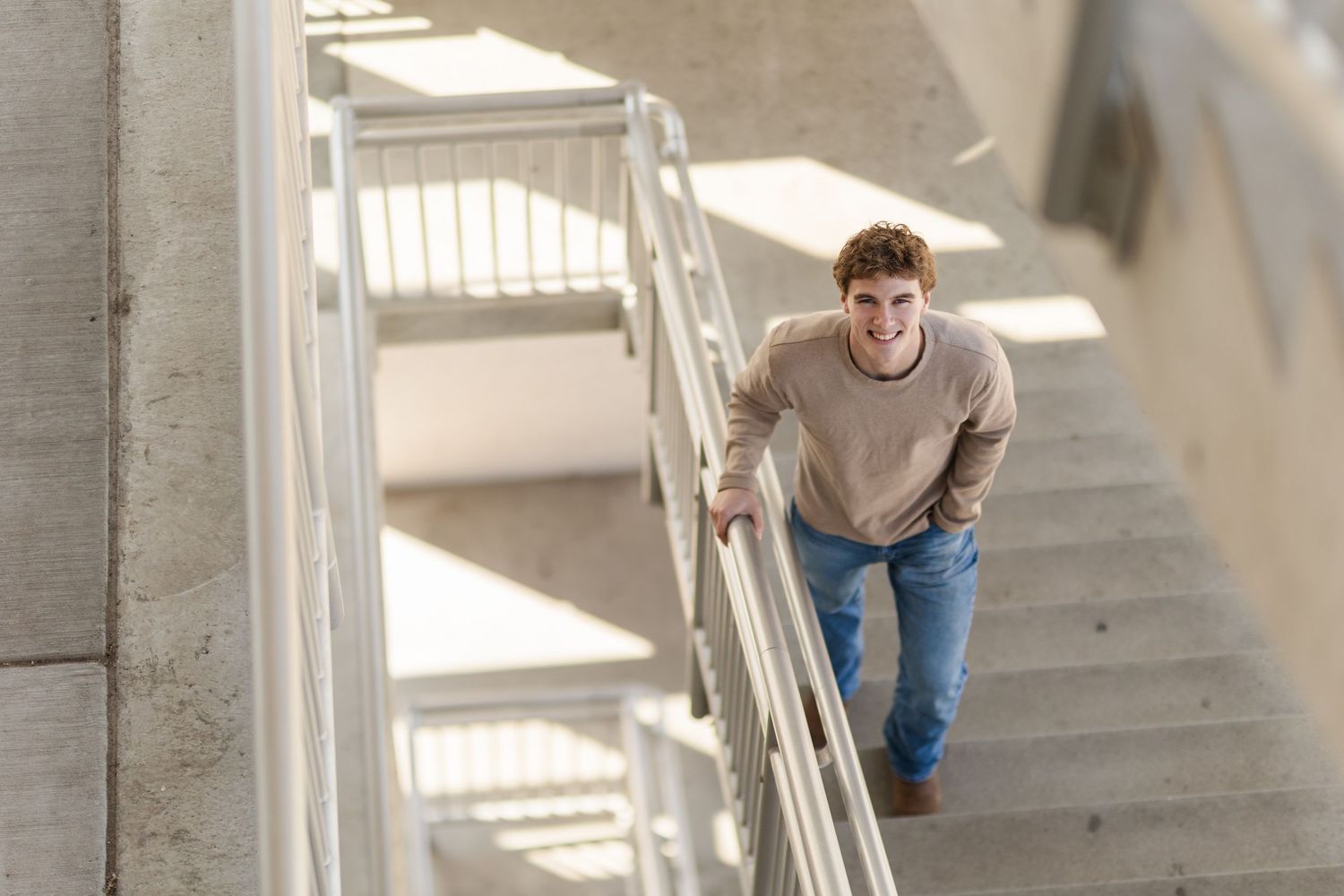 Person in casual wear walking up concrete stairs in bright sunlight.