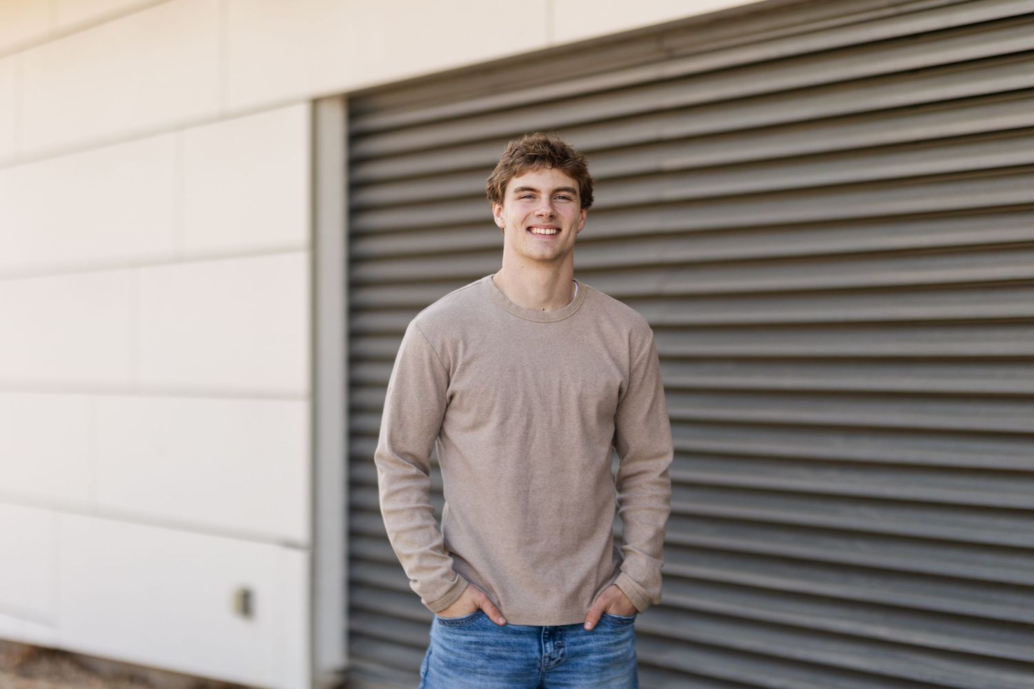 Person in gray sweater with hands in pockets standing in front of industrial door.