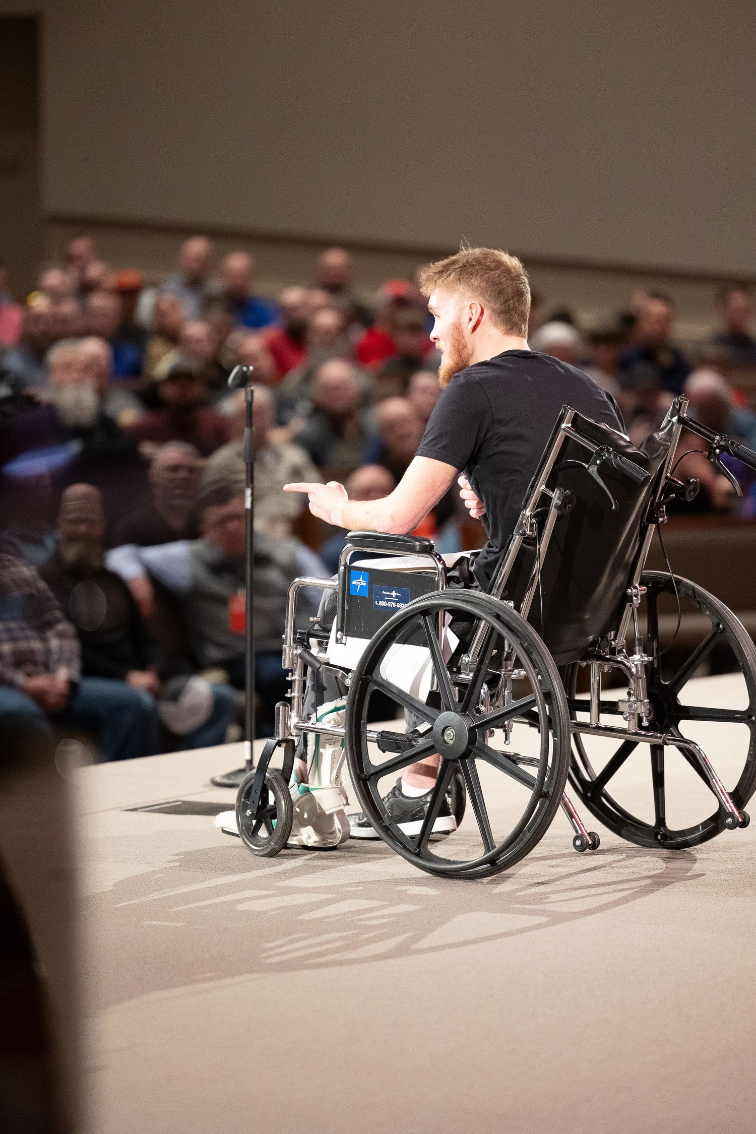 Wheelchair user gives a speech at a podium in front of an audience in an auditorium.