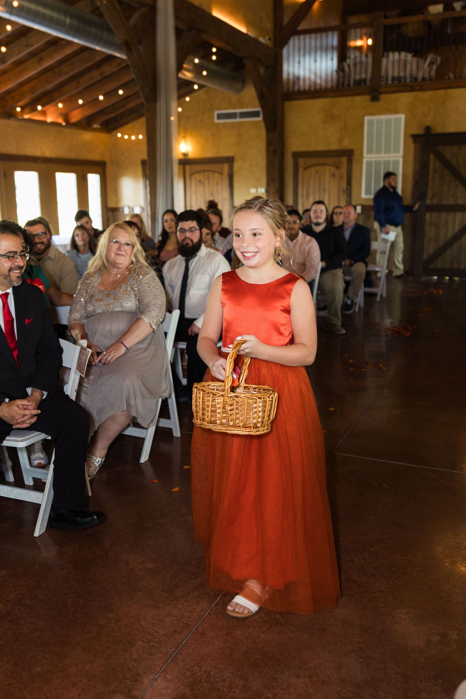 Wedding guests dance and socialize in a rustic barn venue with wooden floors and string lights overhead.