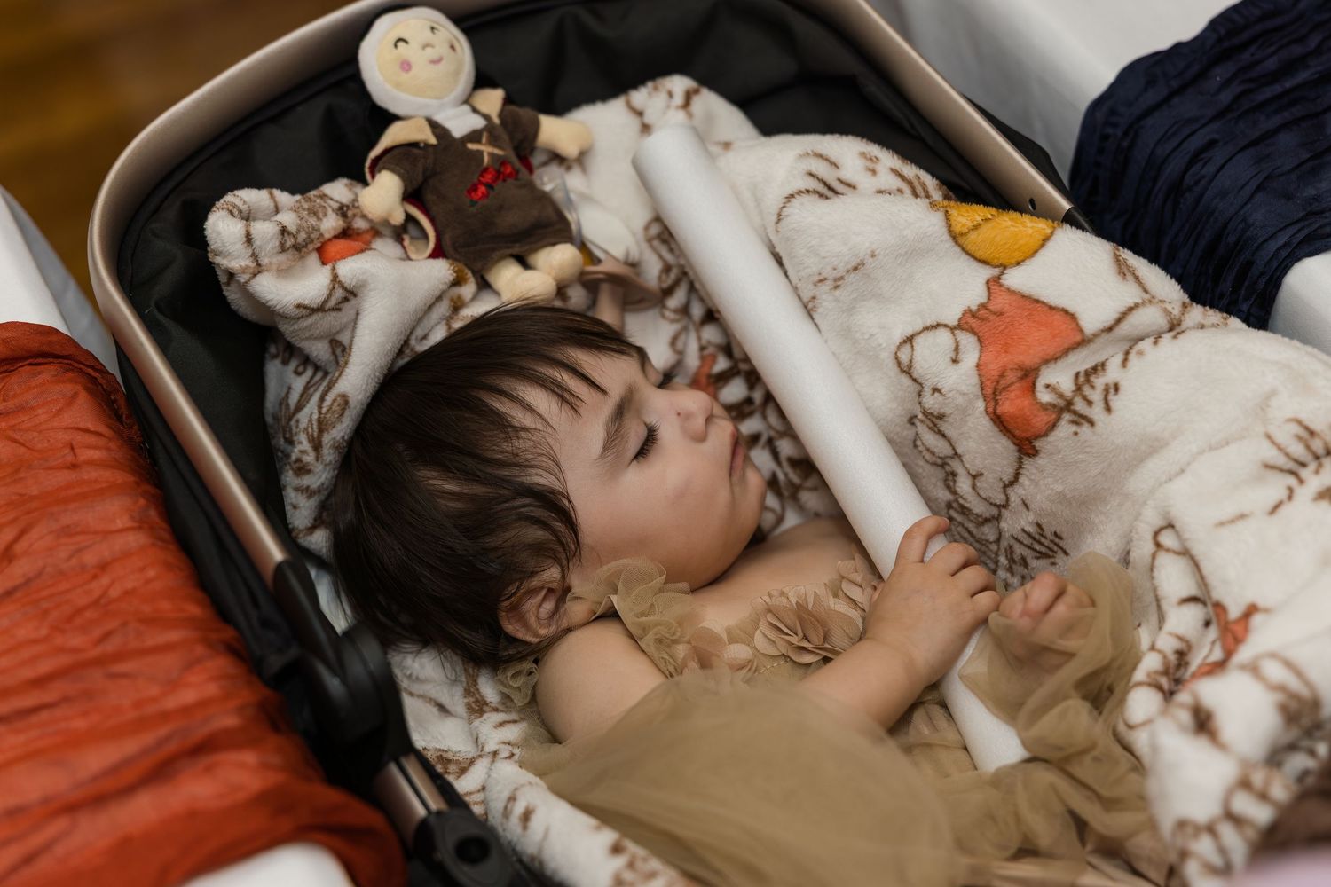 Sleeping toddler lying in stroller surrounded by soft blankets and stuffed animal toys.