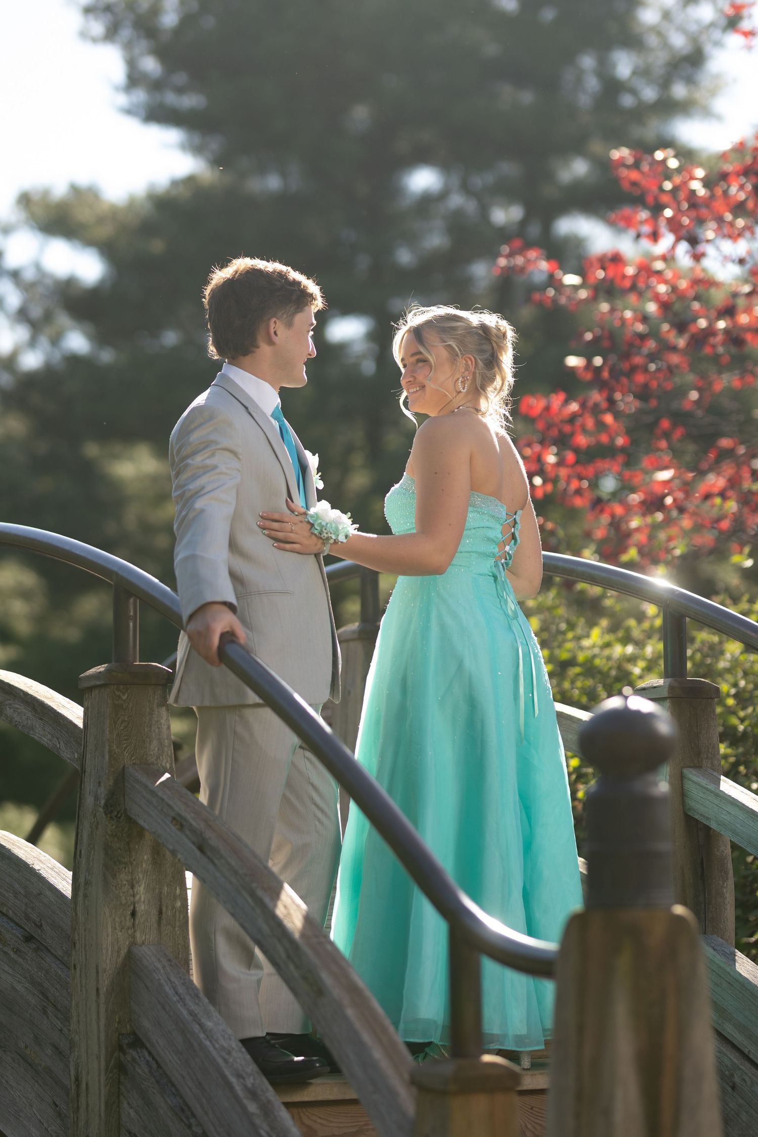 Young couple in formal attire on a wooden bridge, girl in teal gown and boy in gray suit, at prom.