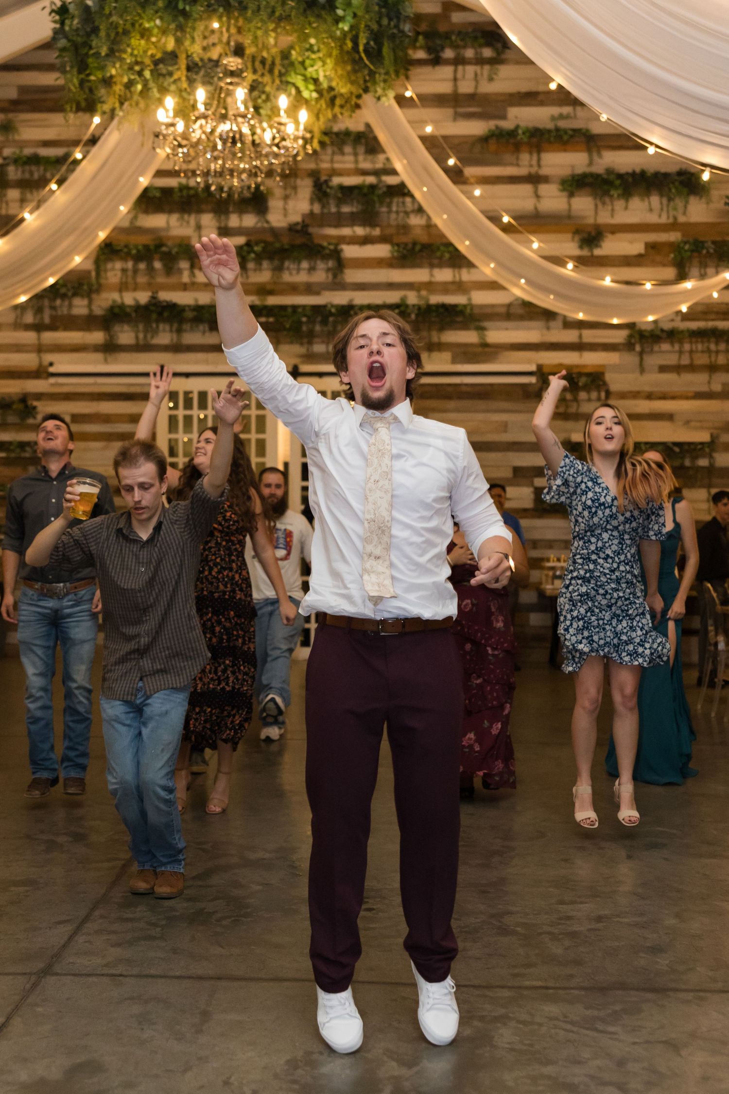 Energetic wedding guest jumping with arms raised on the dance floor.