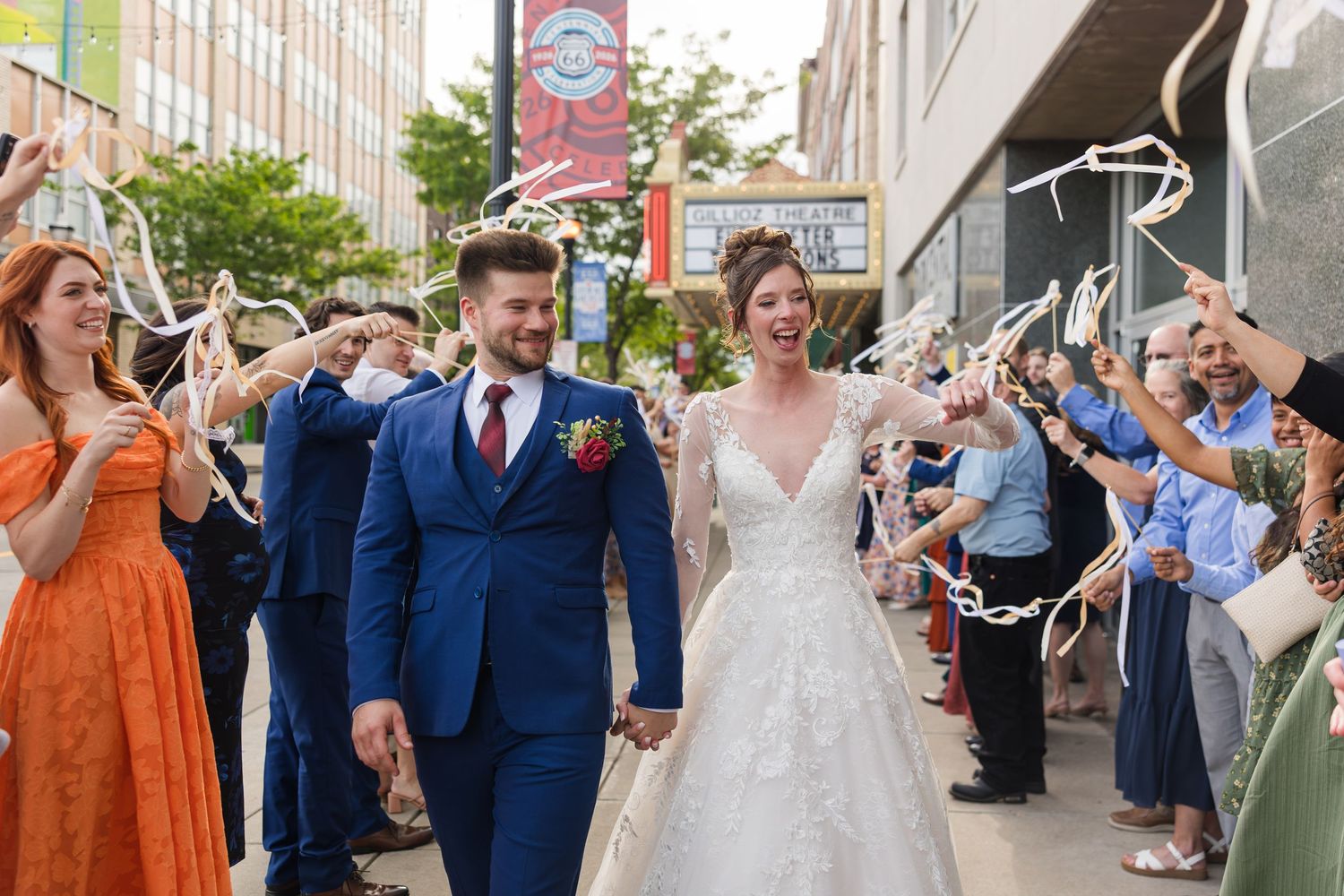 Newlyweds walk hand-in-hand through a joyful ribbon send-off with guests cheering on a city street.