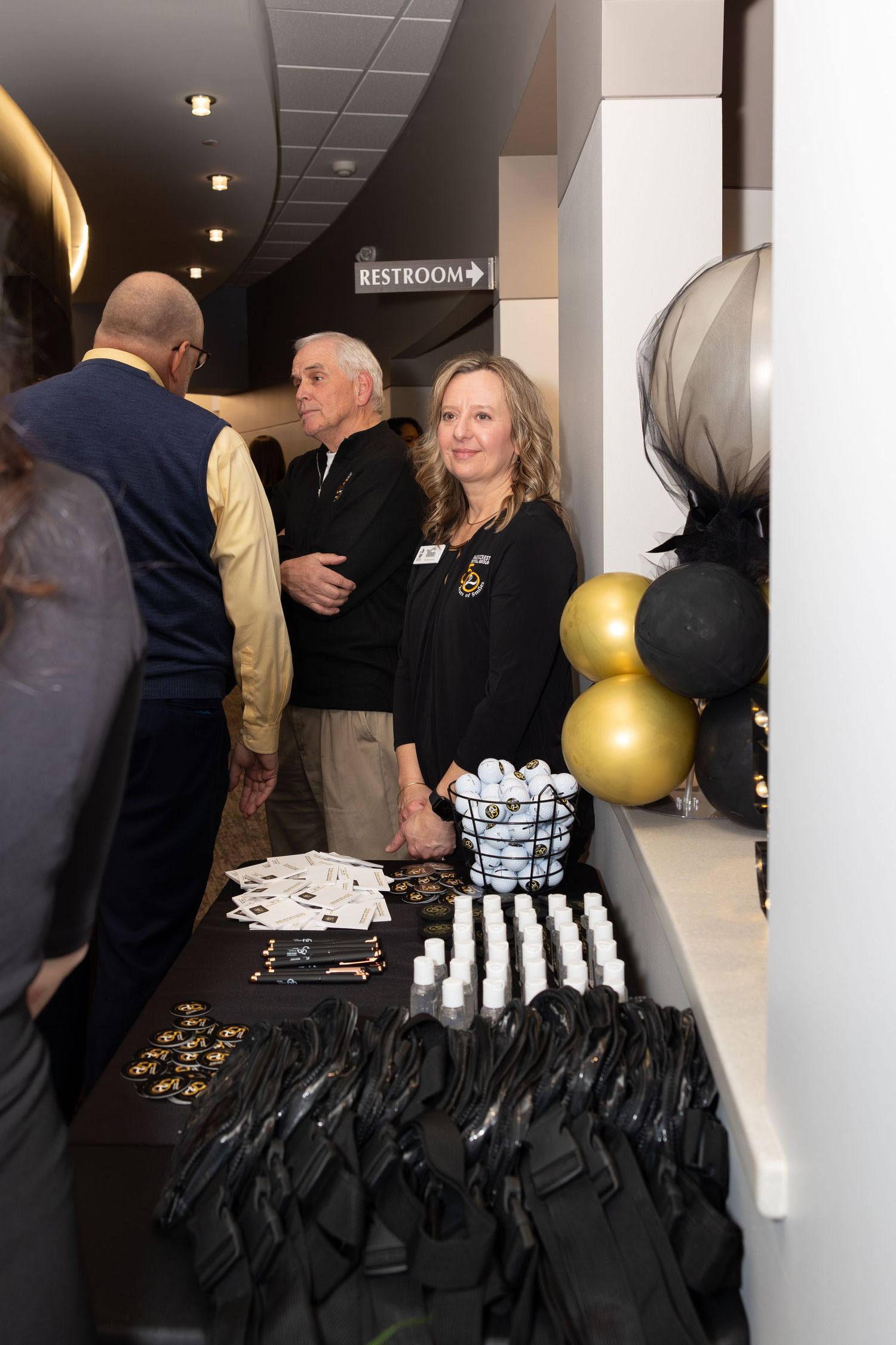 Event merchandise and gift bags displayed on a table with gold balloon decorations.