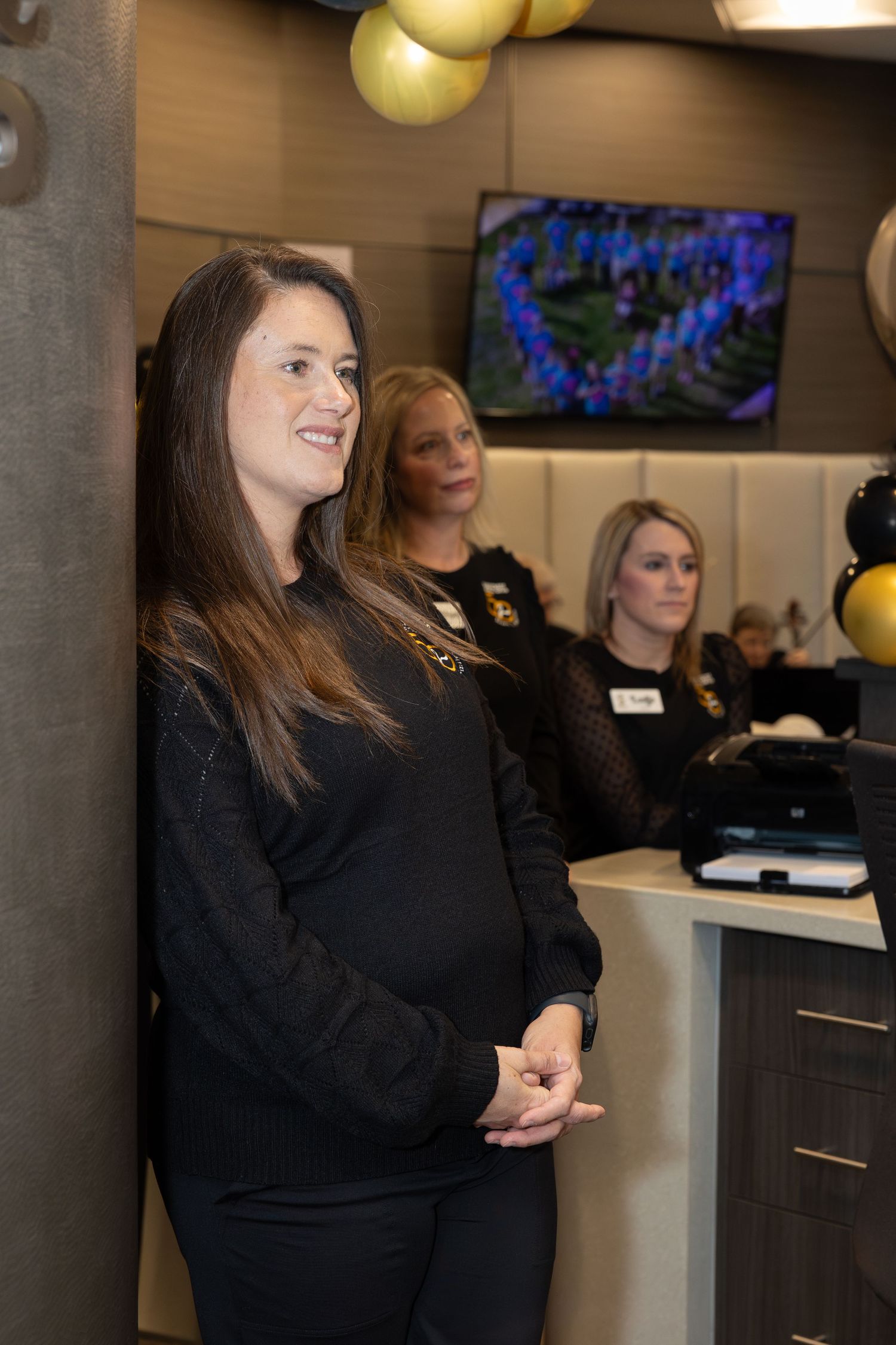 Staff members in black uniforms stand together at an office celebration with decorative balloons.