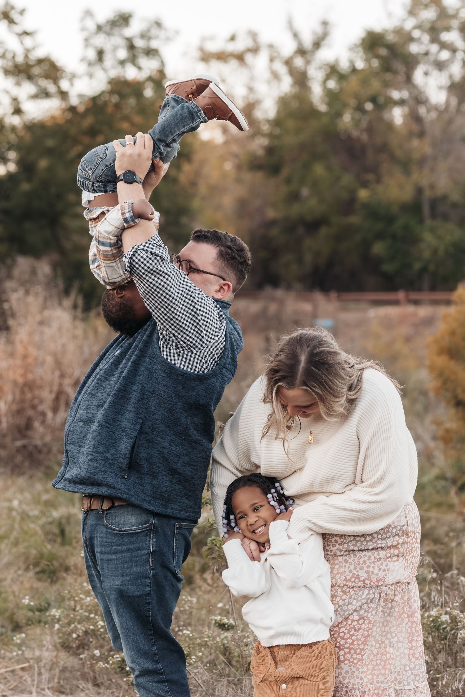A family shares a playful outdoor moment together during a fall photo session in a natural setting.