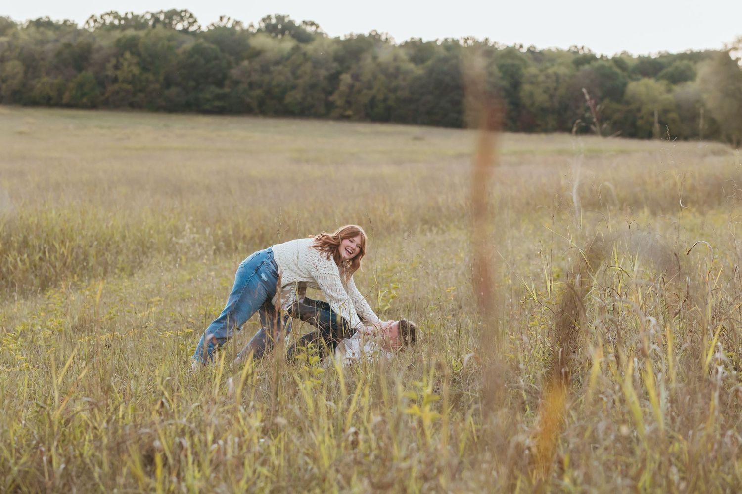 Person in casual attire stooping down in a rustic autumn field.